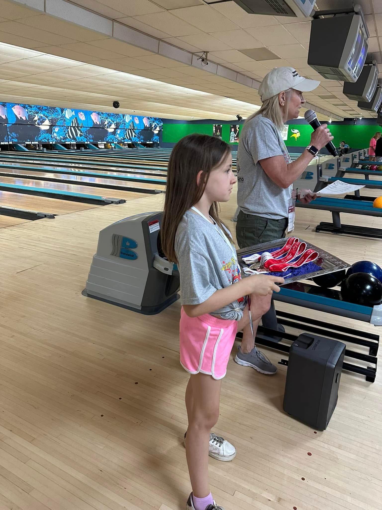 A woman and a little girl are standing in a bowling alley.