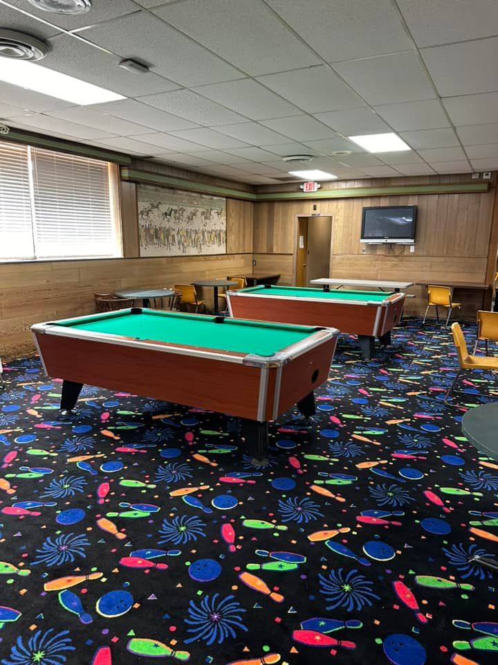 Two pool tables are sitting in a room with a colorful carpet.