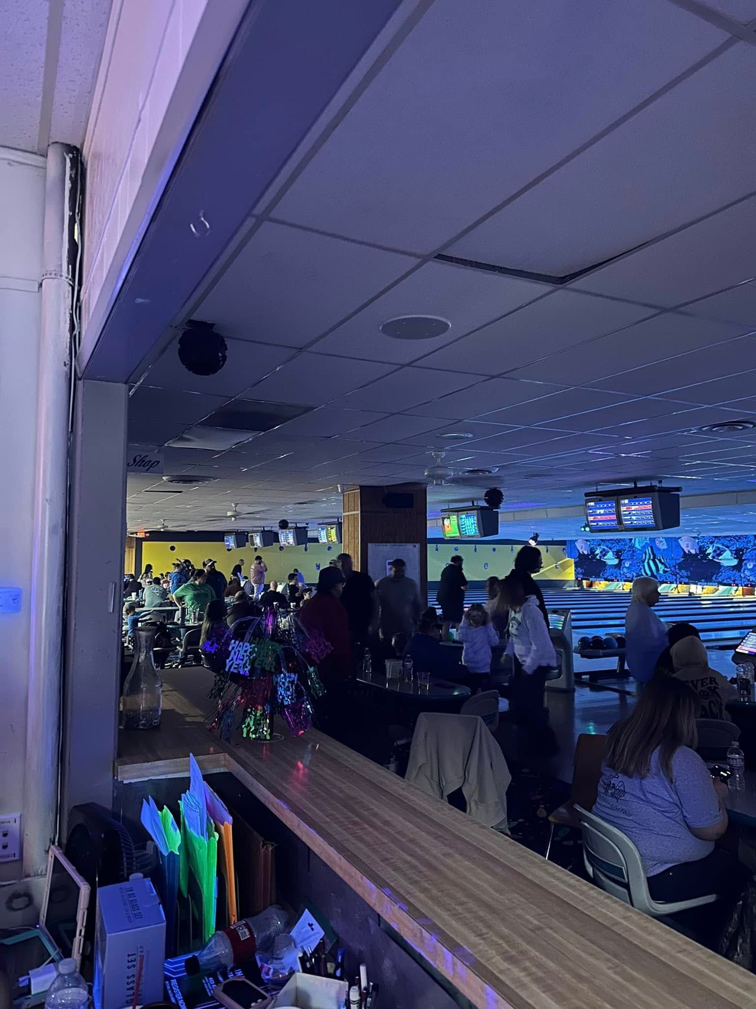 A group of people are sitting at tables in a bowling alley.