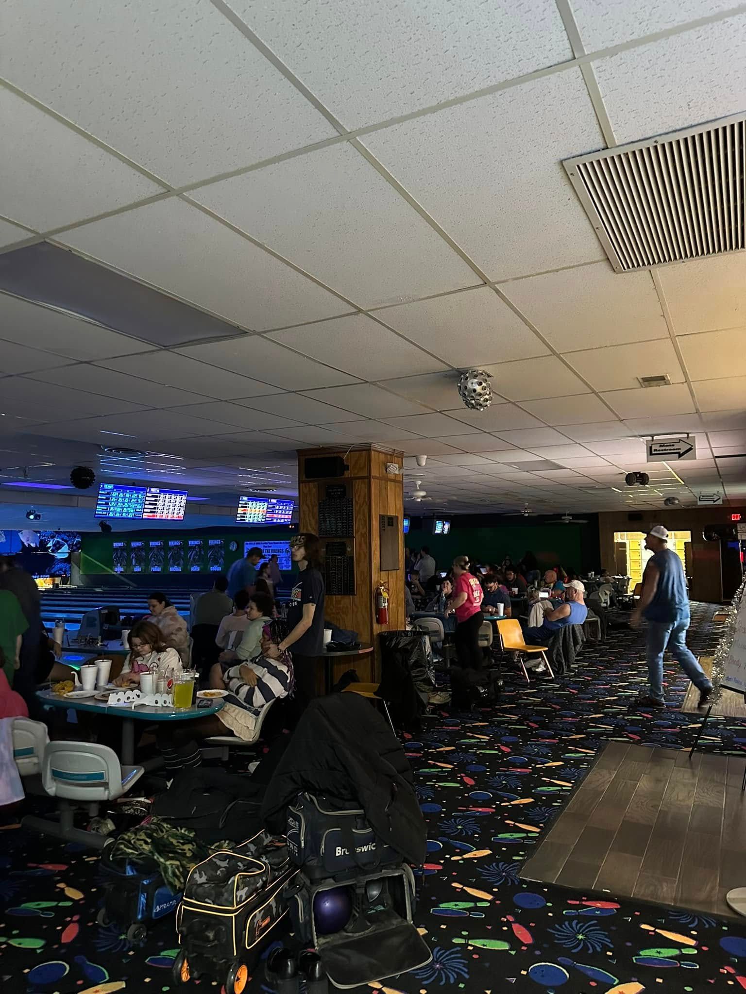 A group of people are sitting at tables in a bowling alley.