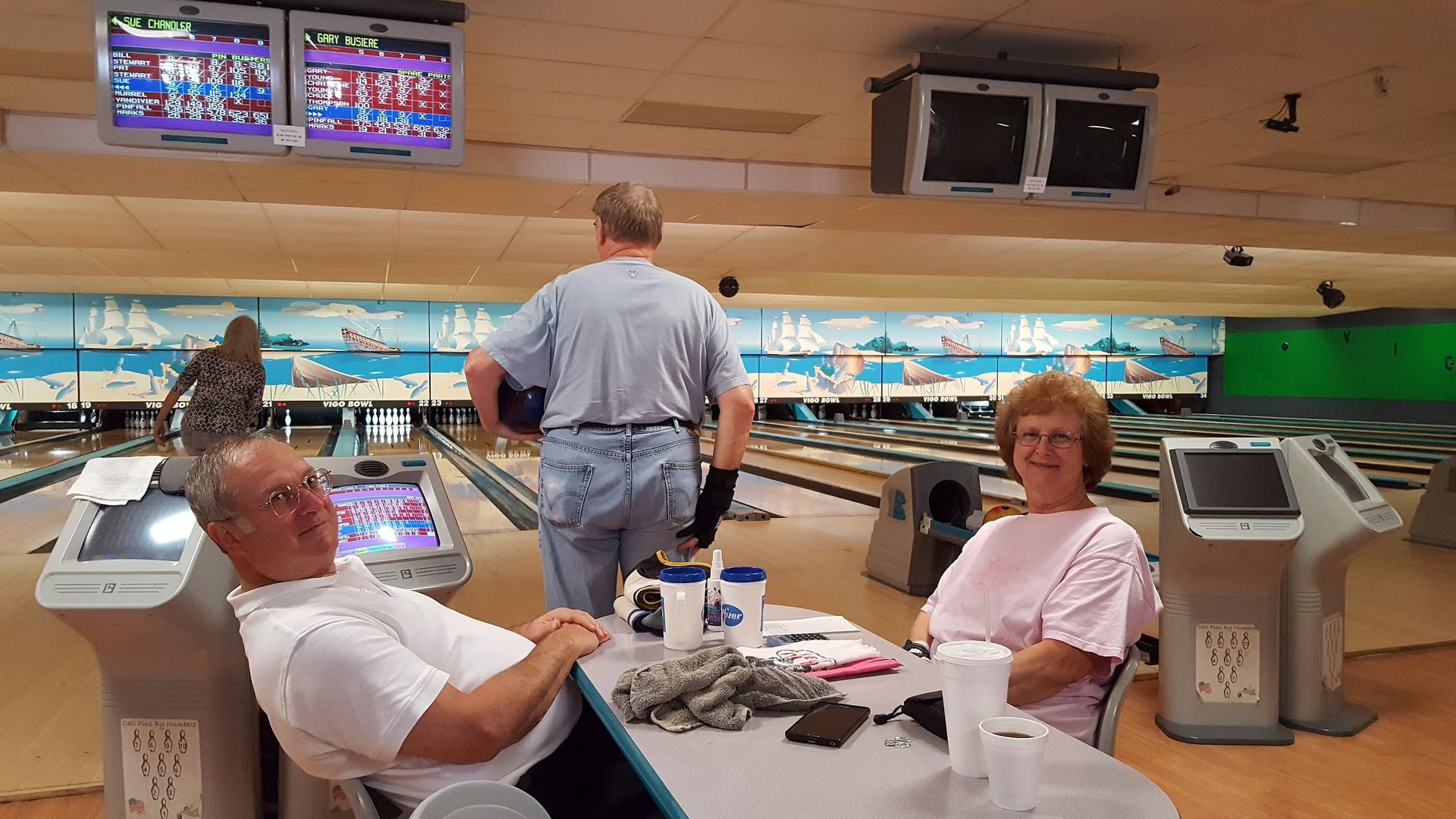A man and a woman are sitting at a table in a bowling alley.