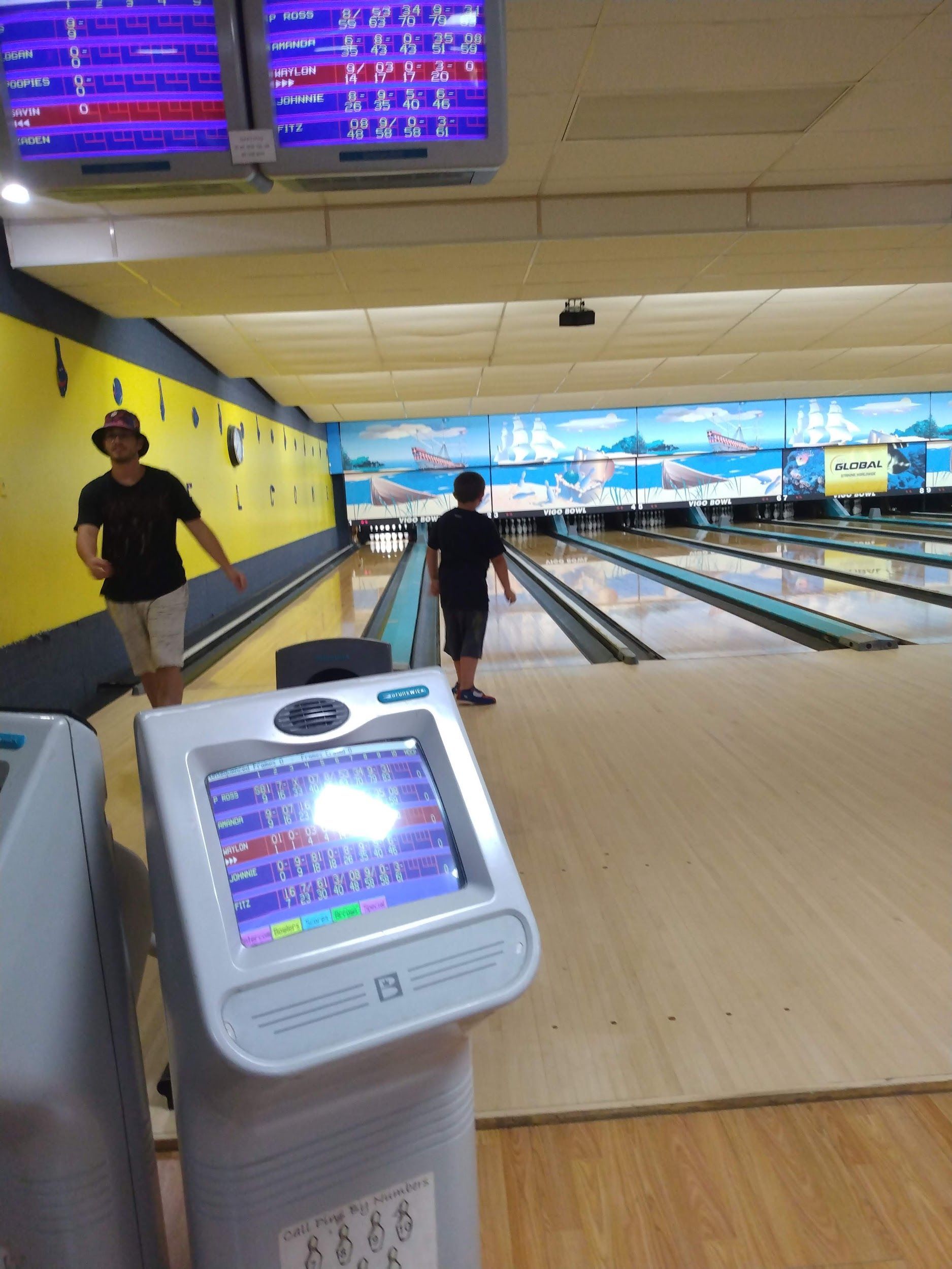A man walking down a bowling alley next to a machine