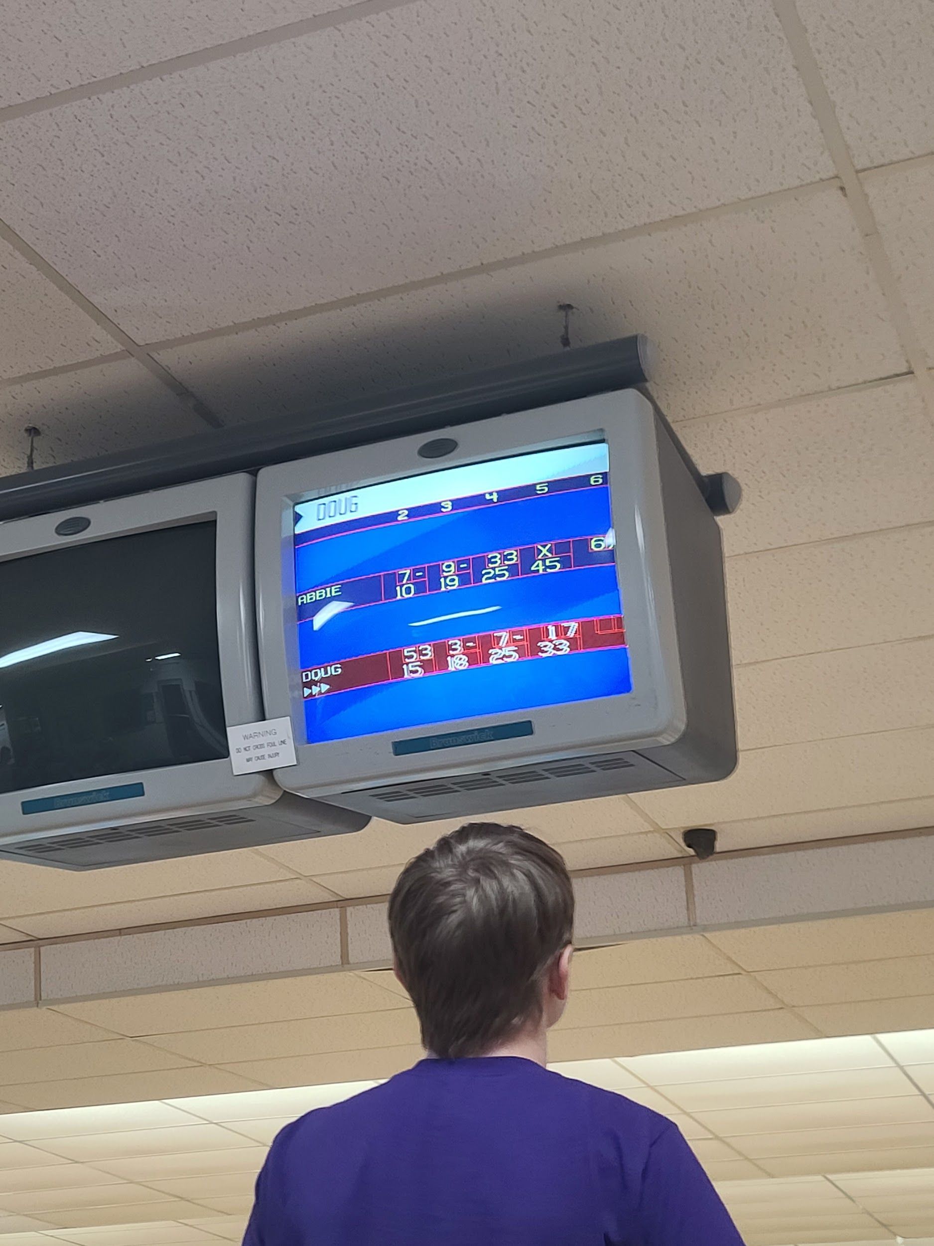 A man in a purple shirt is watching a bowling game on a television