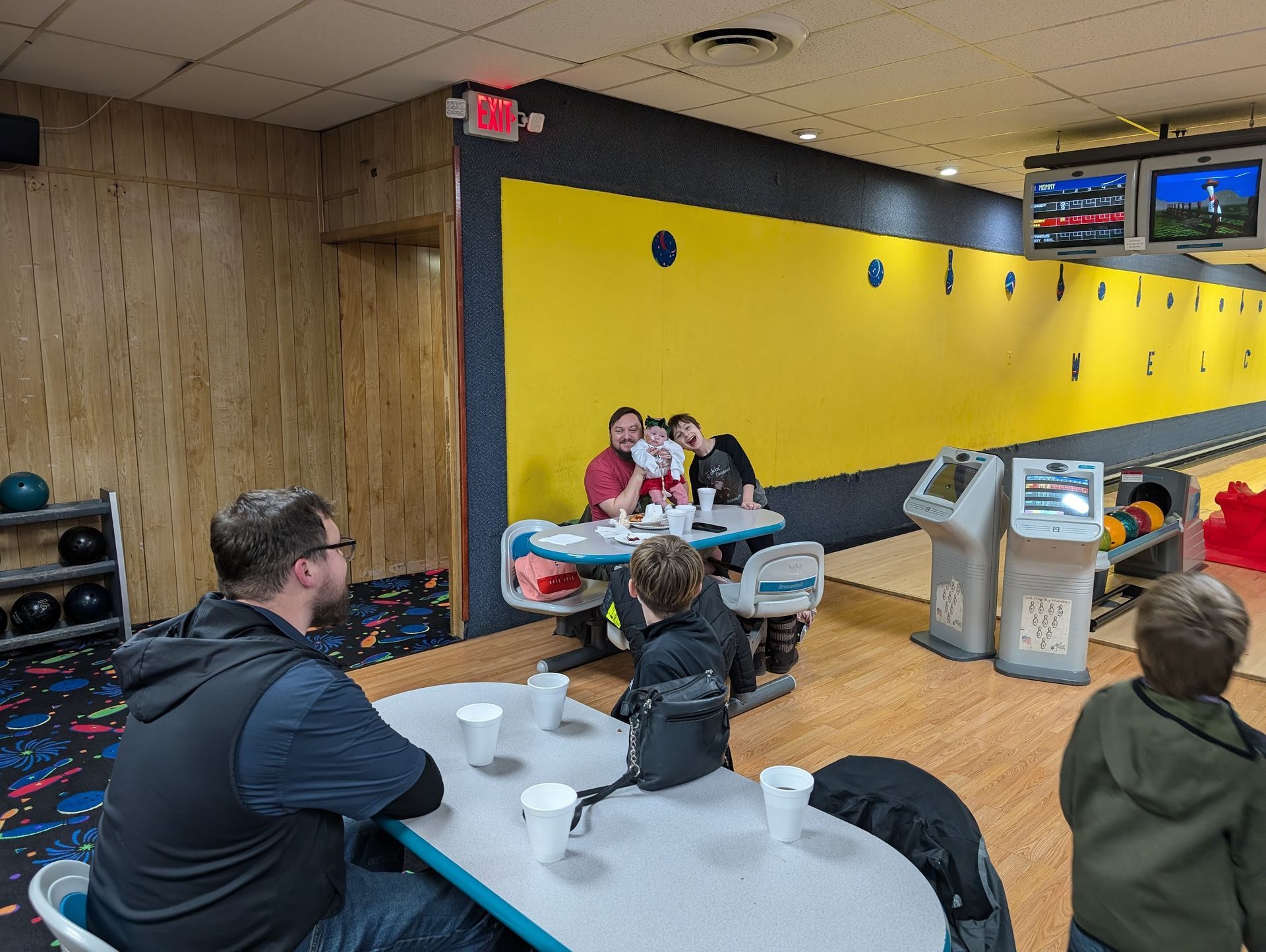 A group of people are sitting at tables in a bowling alley.