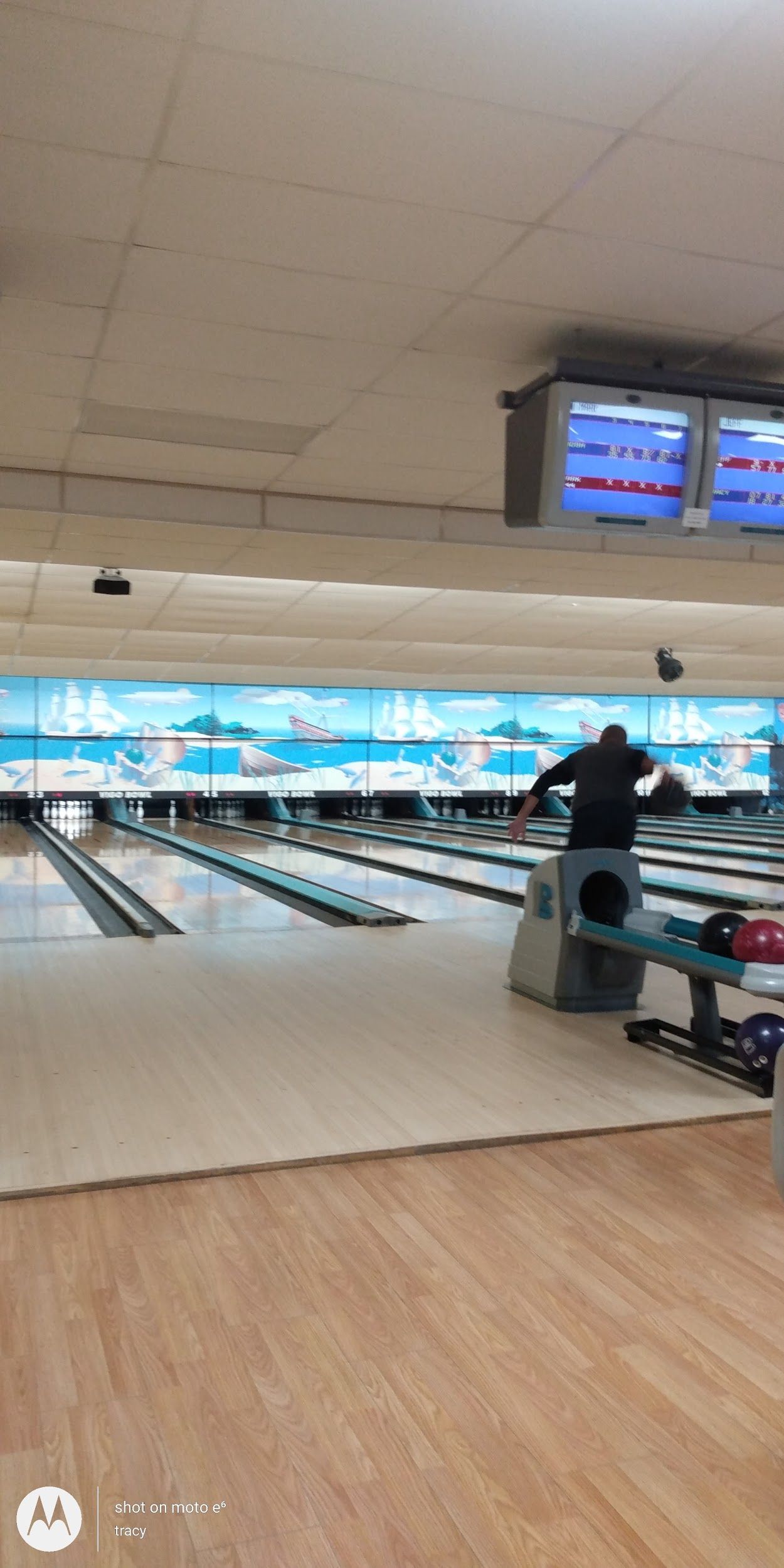 A man is standing on a bench in a bowling alley.