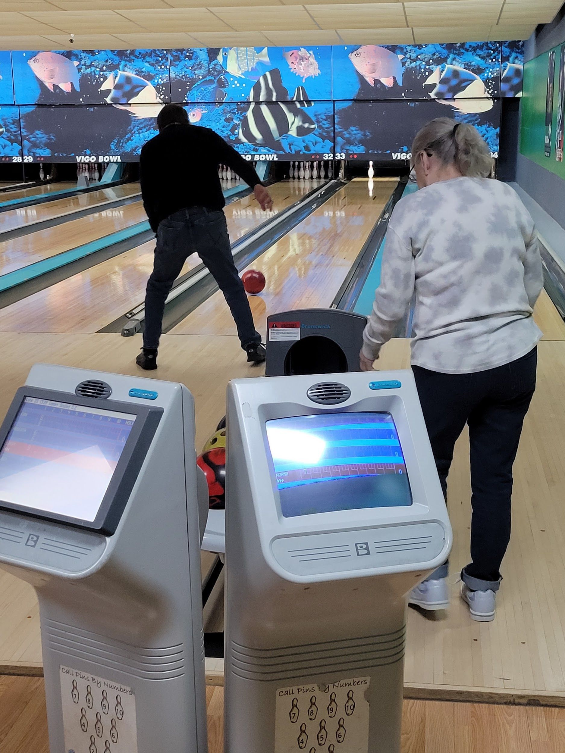 A man and a woman are bowling in a bowling alley