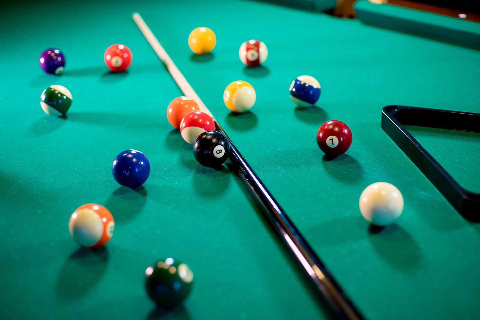 Pool balls scattered on a green billiards table with cues and a black phone