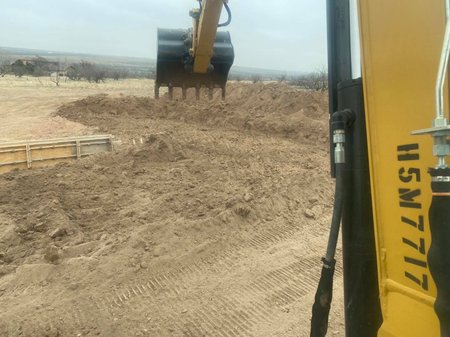 Yellow excavator scooping dirt at a construction site on a brown, dusty terrain.