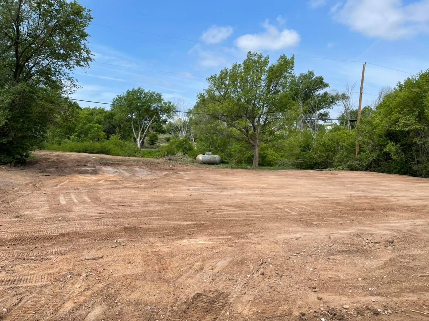 Cleared dirt lot with trees and blue sky in background.