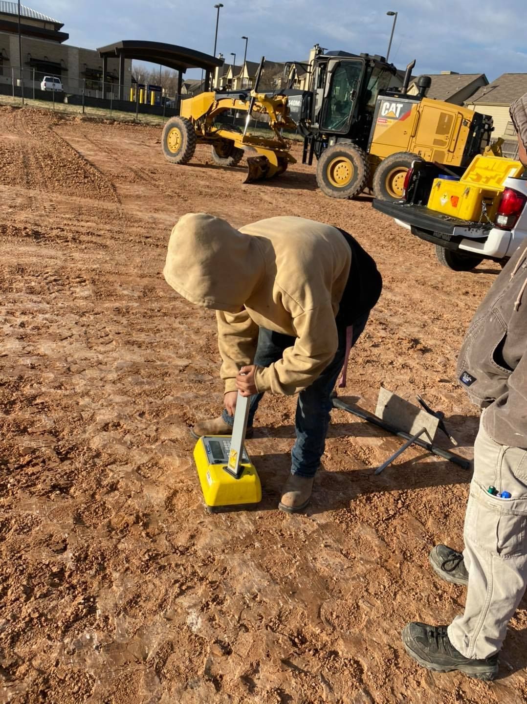 Person in hoodie uses a yellow ground-penetrating radar device on a construction site.