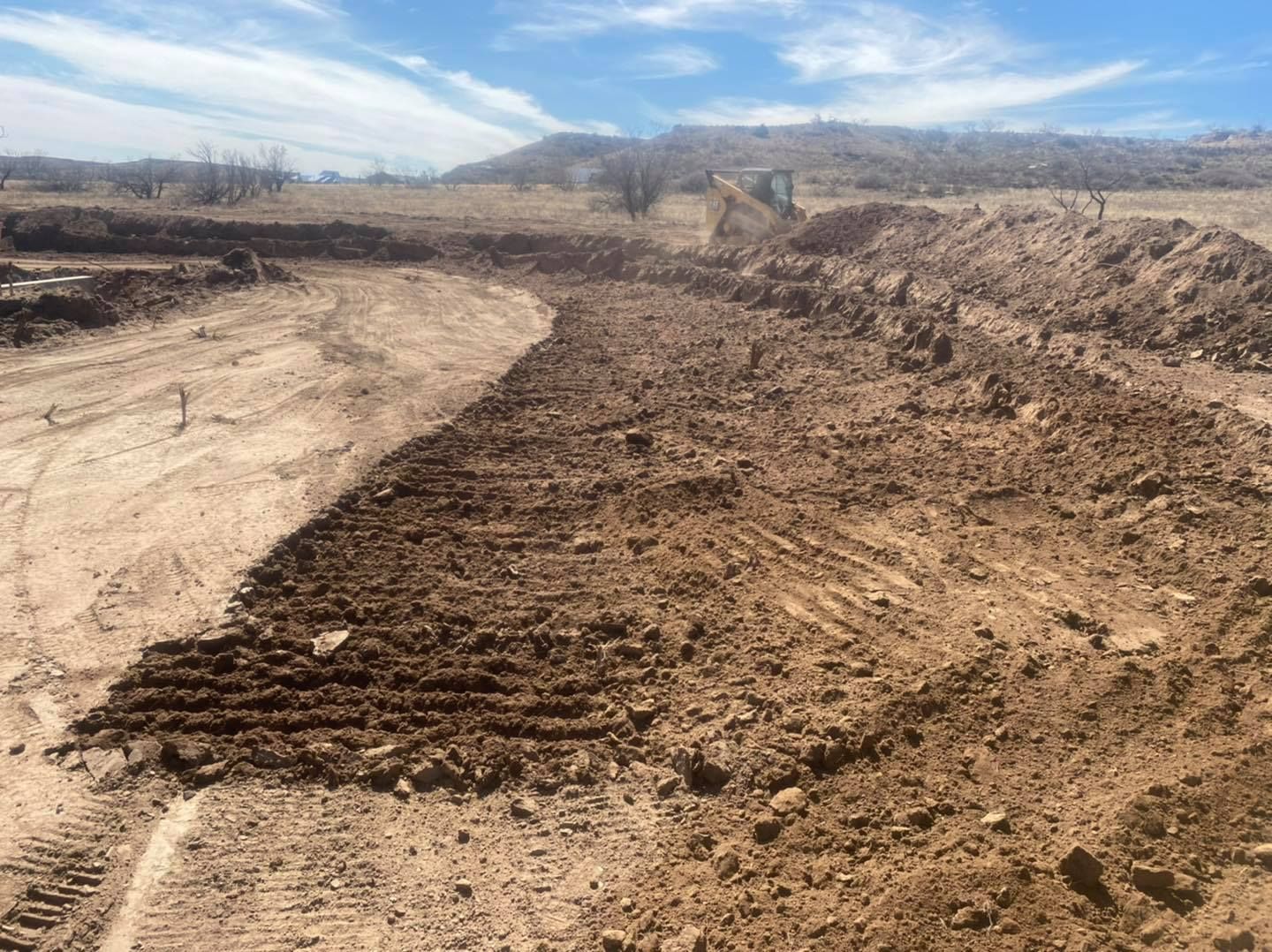 Dirt and soil on construction site, with a hill in the background under a blue sky.