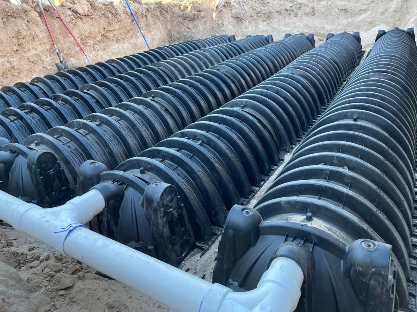 Rows of black septic system modules installed in a trench with white PVC piping.