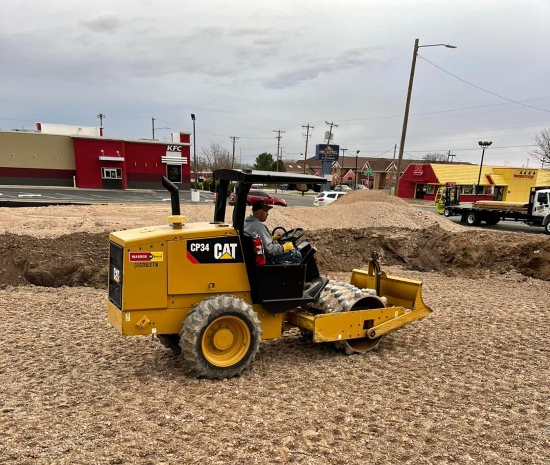 A yellow CAT compact soil compactor driven by a person, operating in a construction area.