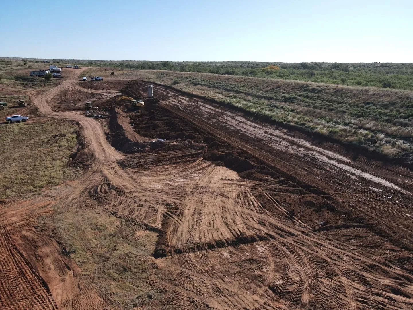 Dirt road and deep trench cut through a barren, muddy field under a clear sky