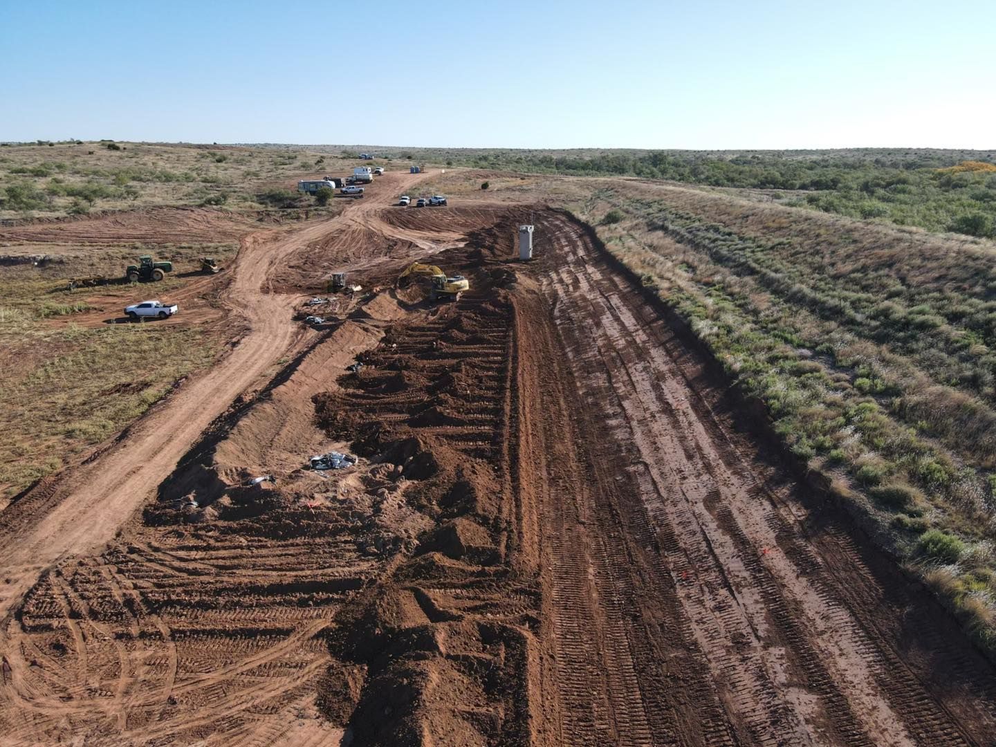 Dirt road under construction in an open field. Vehicles and machinery are present; brown earth dominates.