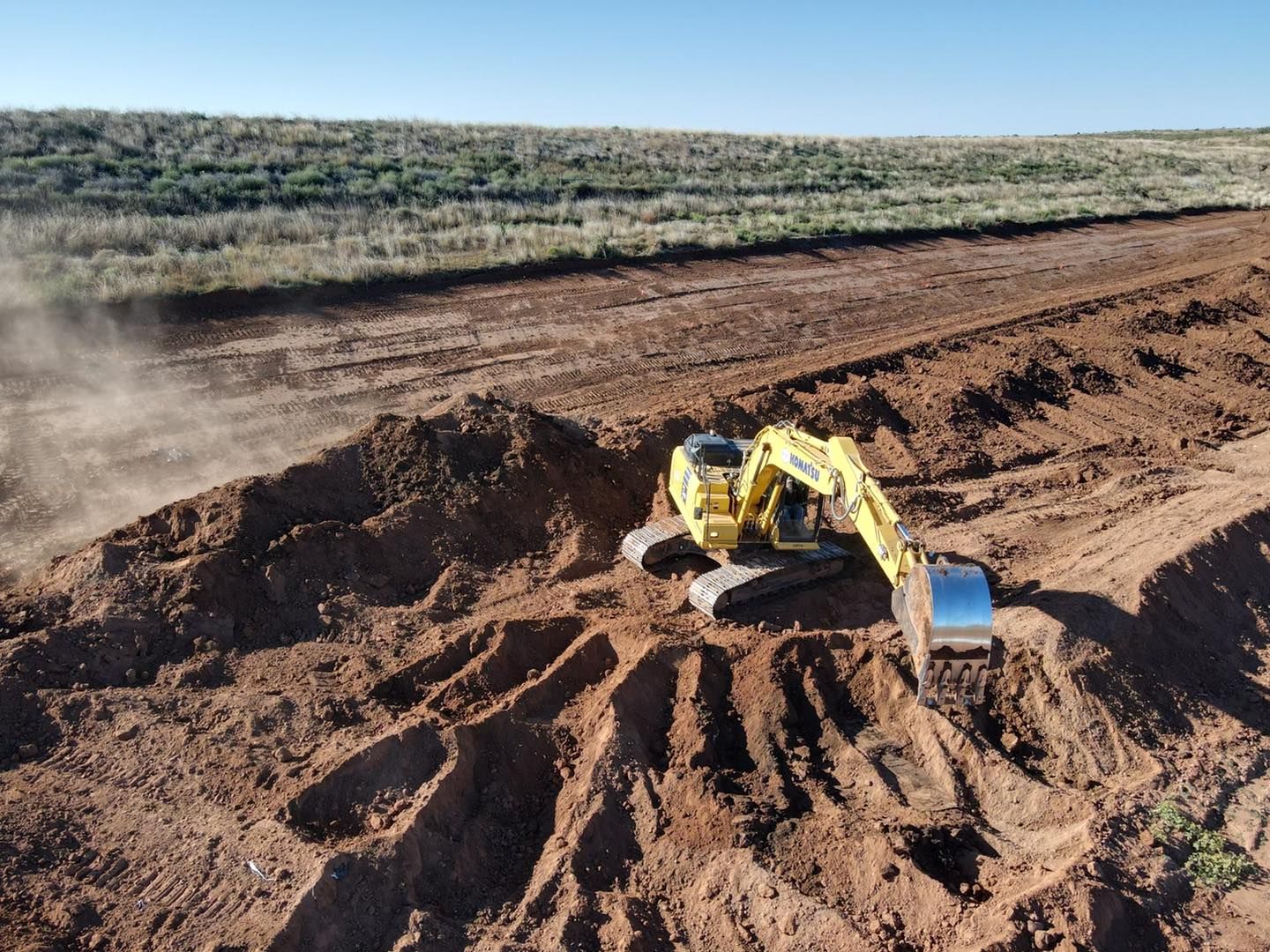 An excavator digs in brown dirt at a construction site under a clear blue sky.