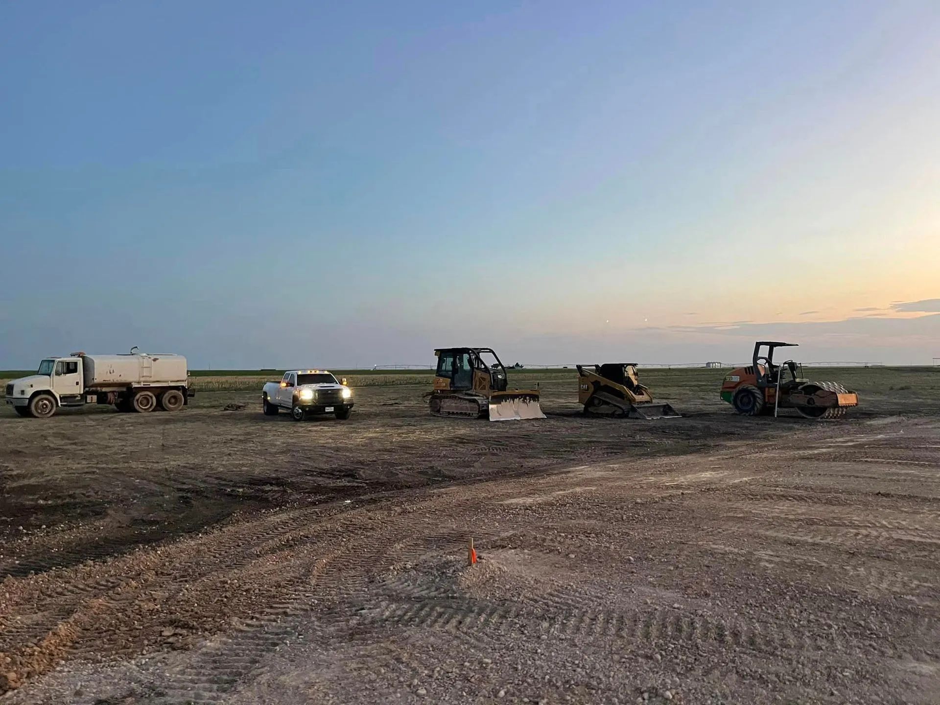 Construction equipment on a flat, barren landscape under a dusky blue sky.