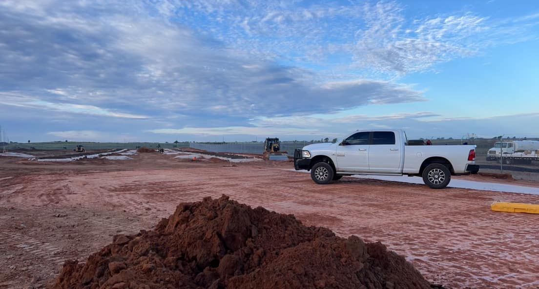 White truck parked on reddish-brown dirt under a cloudy sky. A pile of dirt in the foreground.