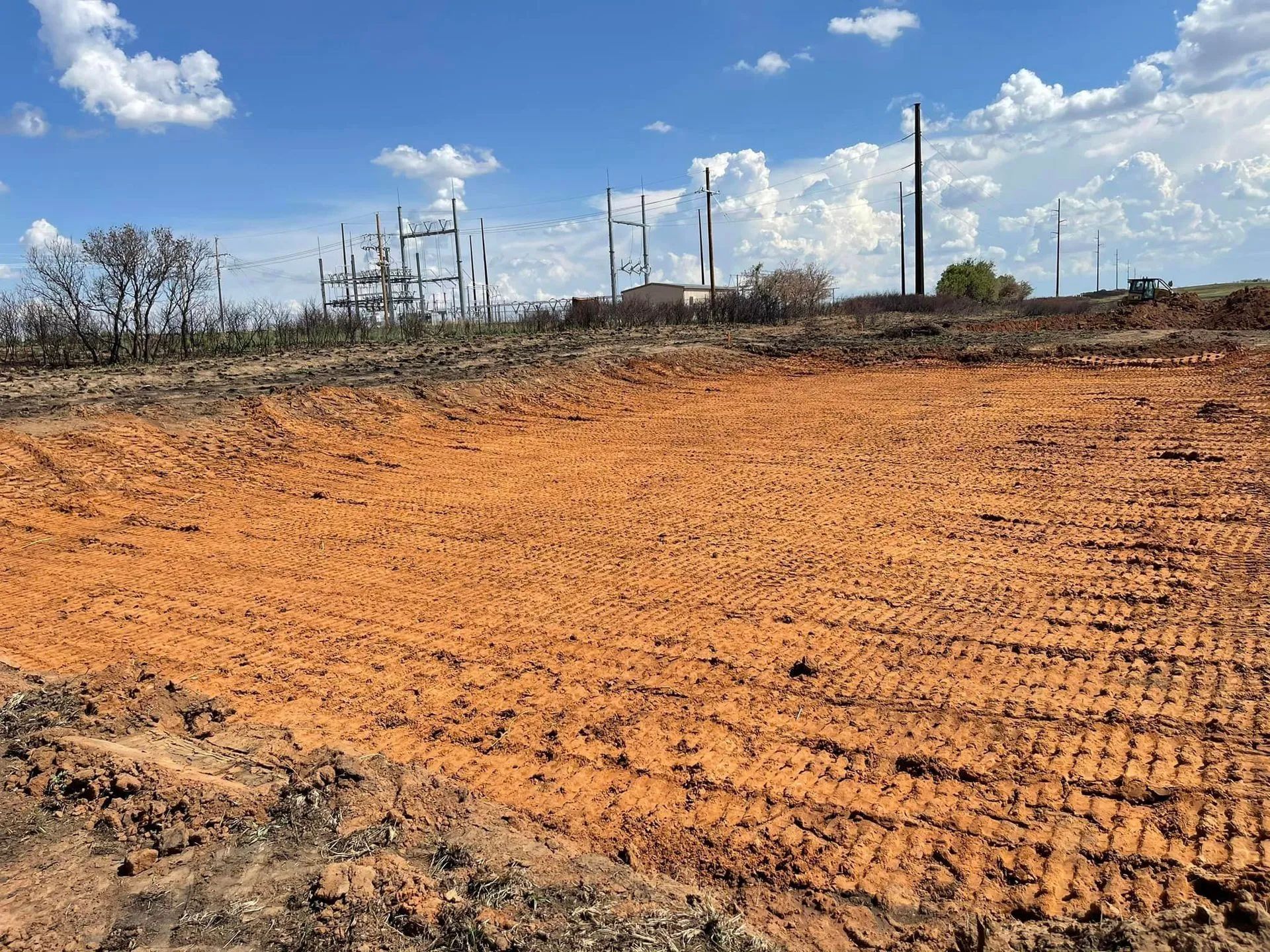 Dirt-covered field with industrial pipes and towers under a bright blue sky with clouds