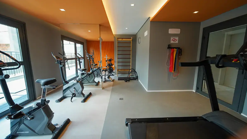 Sala de ginástica com aparelhos de cardio, espelhos de parede e decoração em tons de laranja e cinza.