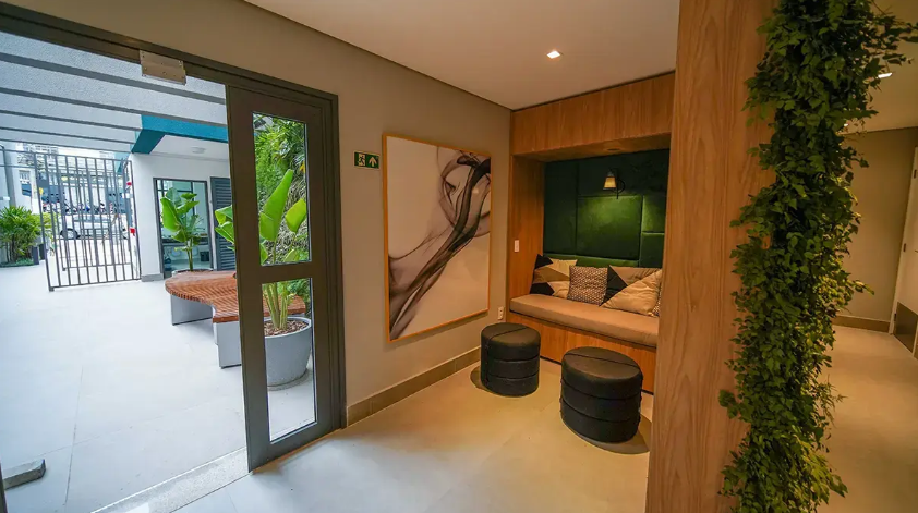 Sala de estar interna moderna com bancos de madeira, plantas em vasos e portas de vidro que se abrem para um pátio iluminado.