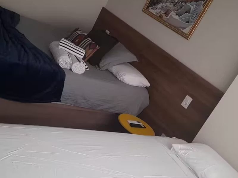Quarto de hotel pequeno com duas camas, toalhas brancas e um telefone amarelo no chão perto da parede.