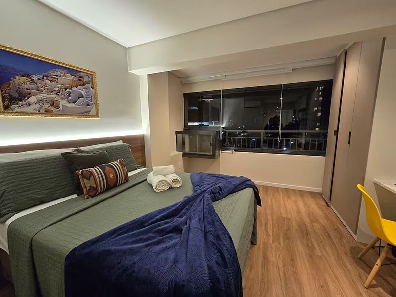 Quarto de hotel moderno com cama, janela grande, escrivaninha e cadeira amarela.