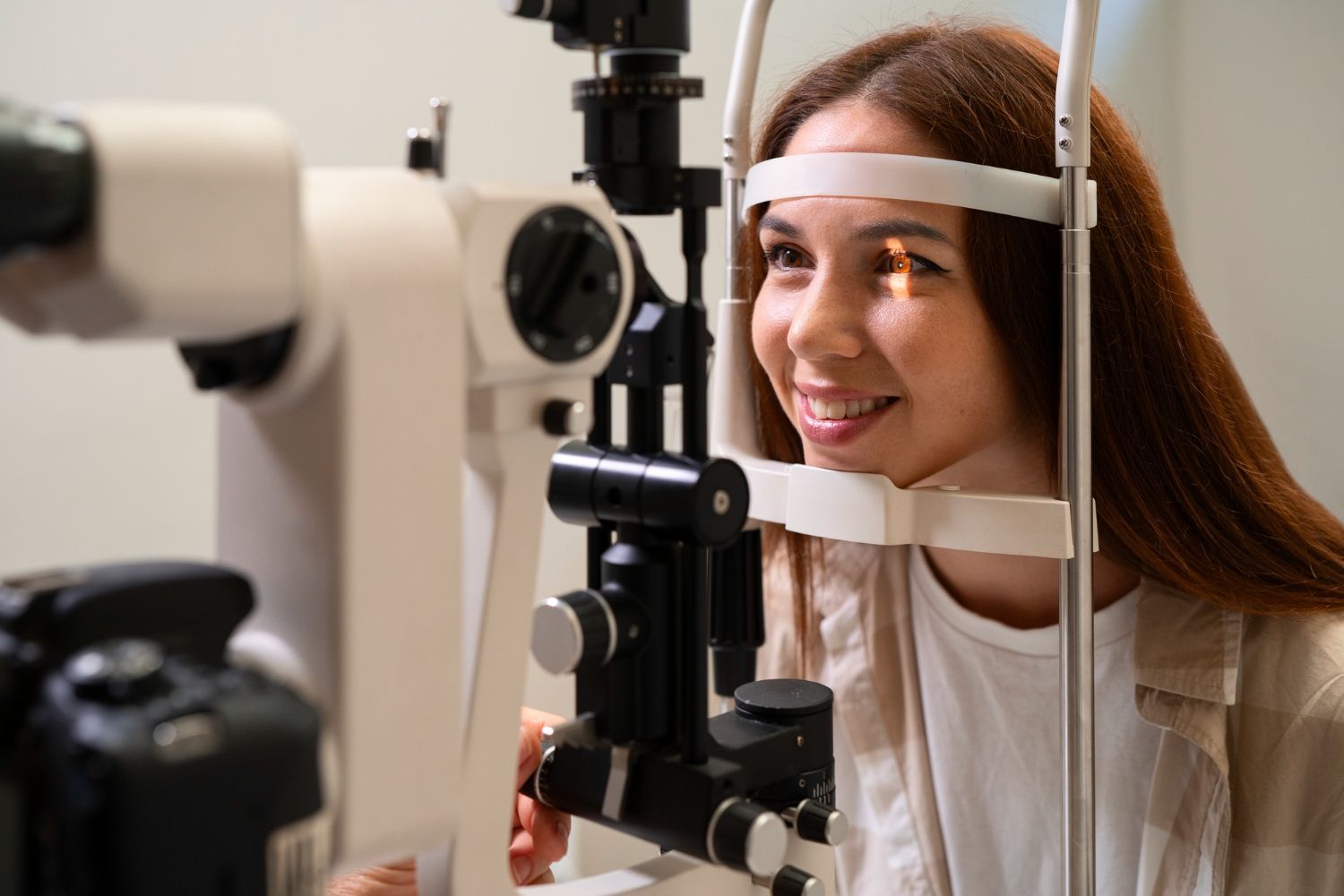 Woman having an eye exam with a slit lamp machine, smiling, indoors.