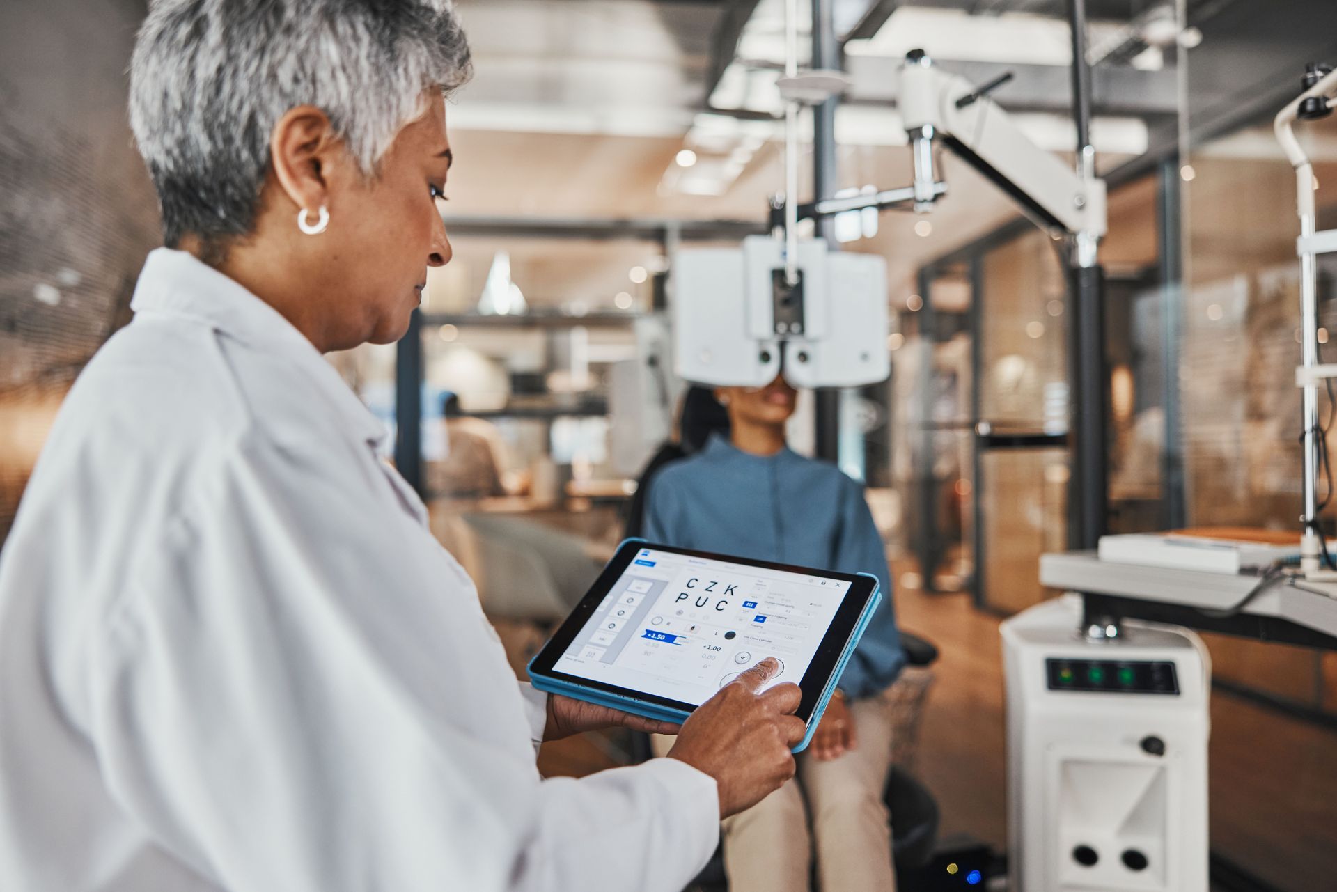 Person in a lab coat using a tablet beside industrial machinery in a manufacturing lab