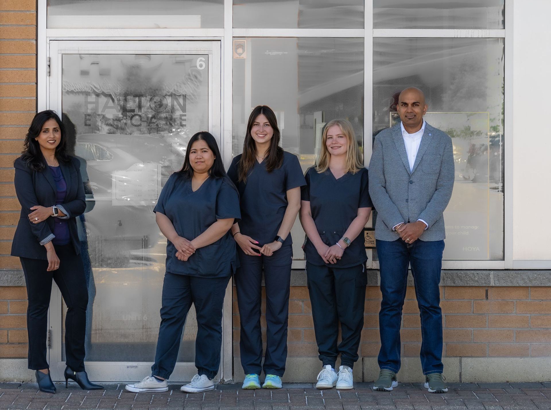 Five people stand in front of a building entrance, posing for a group photo.