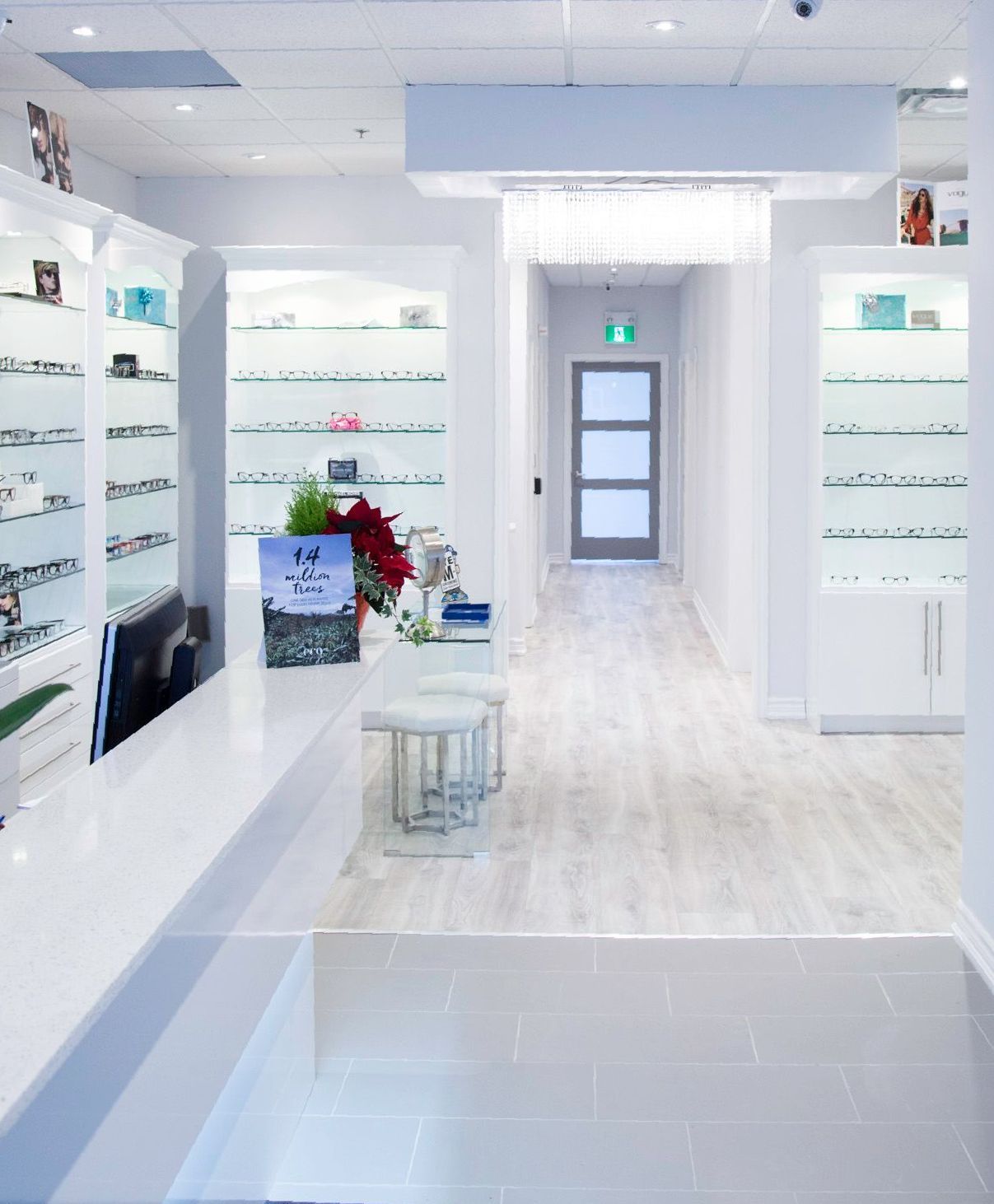Bright white eyewear shop interior with display shelves and a doorway at the back.