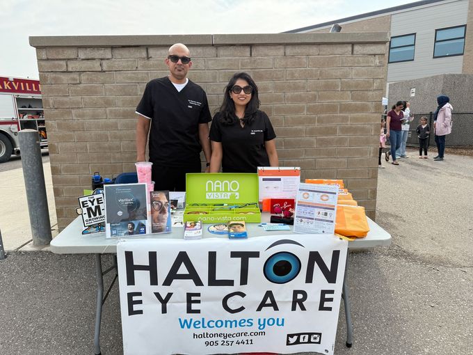 Halton Eye Care booth with two staff behind a table of promotional items outdoors