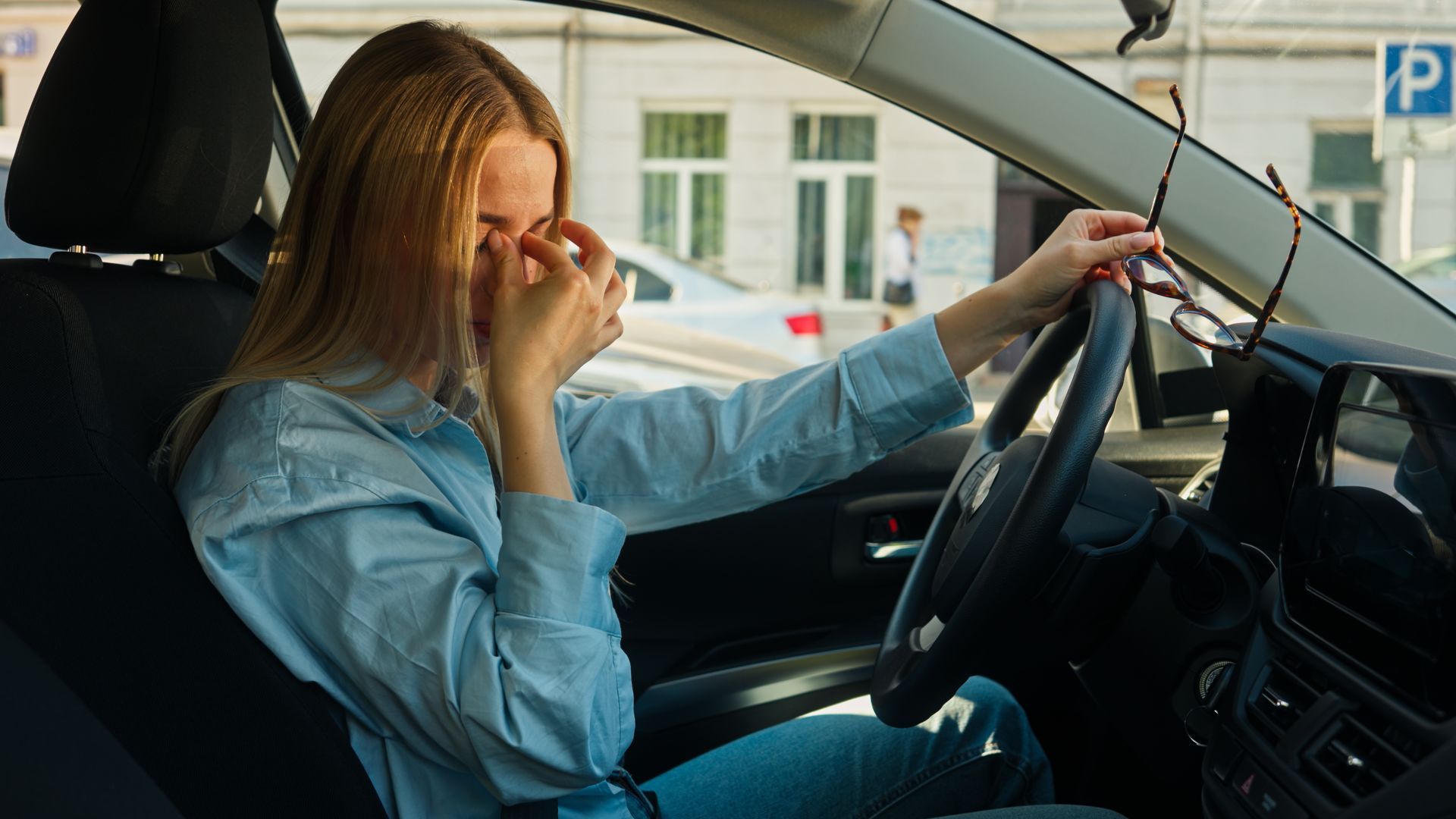 Woman driving a car while rubbing her eye with her left hand