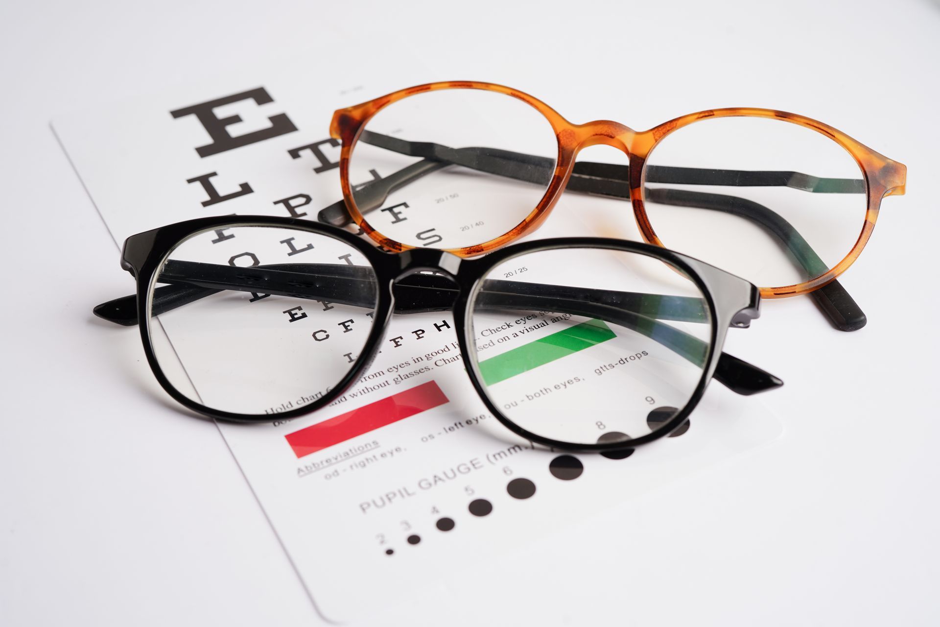 Three eyeglasses frames on a vision test chart, including black, tortoiseshell, and black-rimmed styles