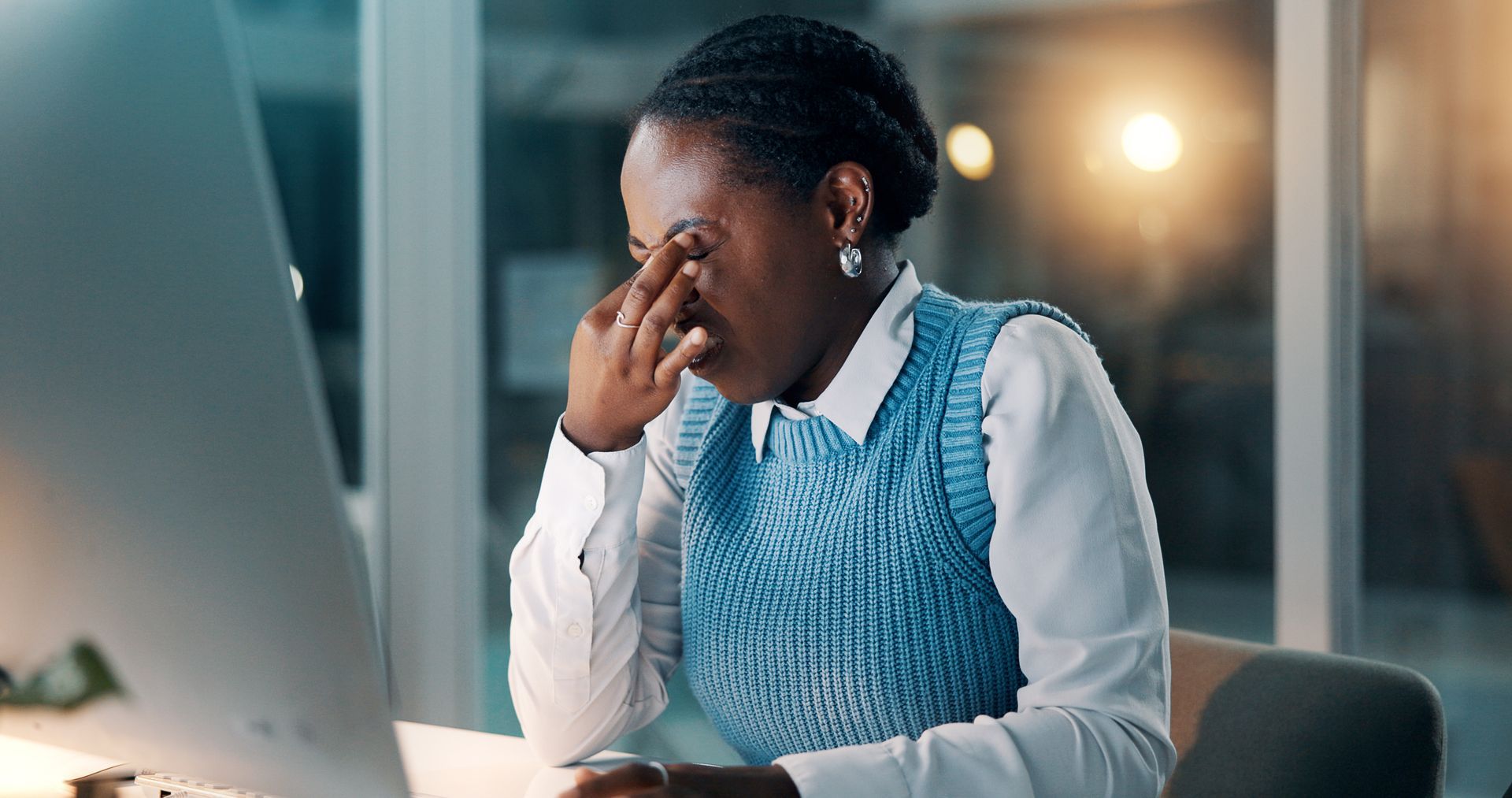 Tired office worker rubbing eyes at a desk with a laptop in a dimly lit room