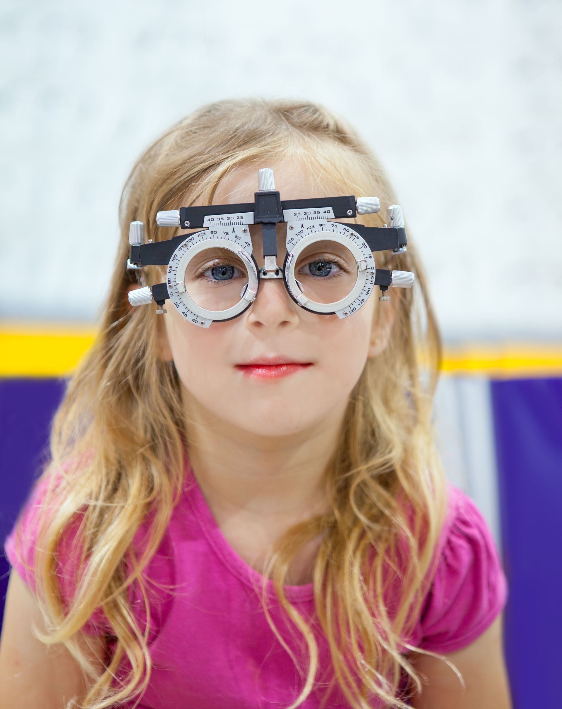 Child wearing novelty glasses with fake nose, standing against a blurred indoor background.