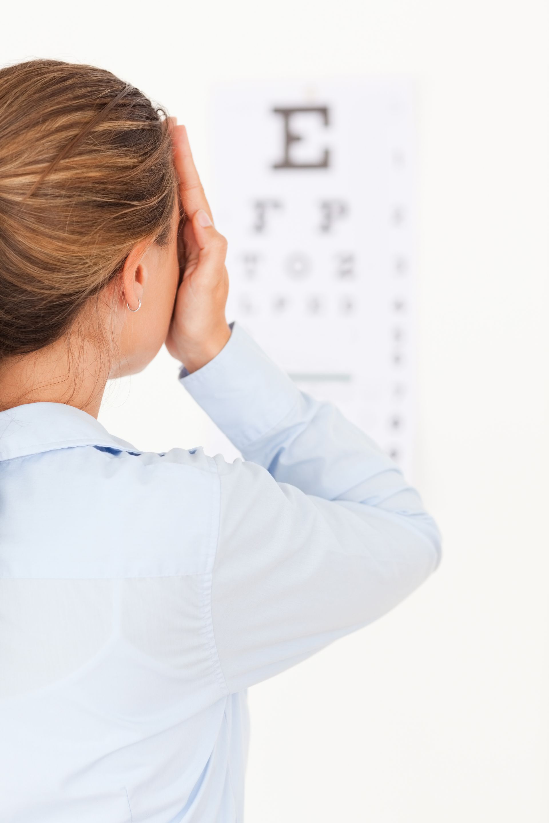Person covering one eye during an eye exam with vision chart in the background