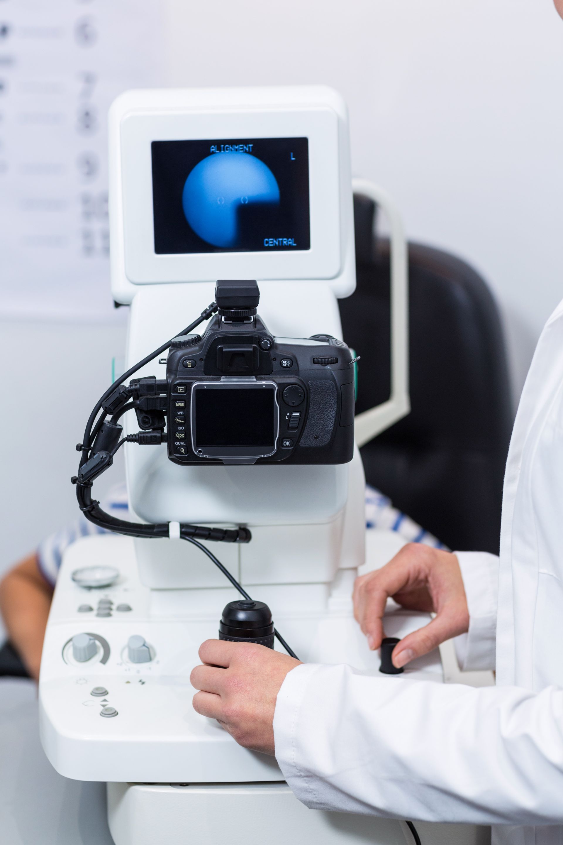 Person adjusting a camera mounted on an eye-testing machine with a blue screen display