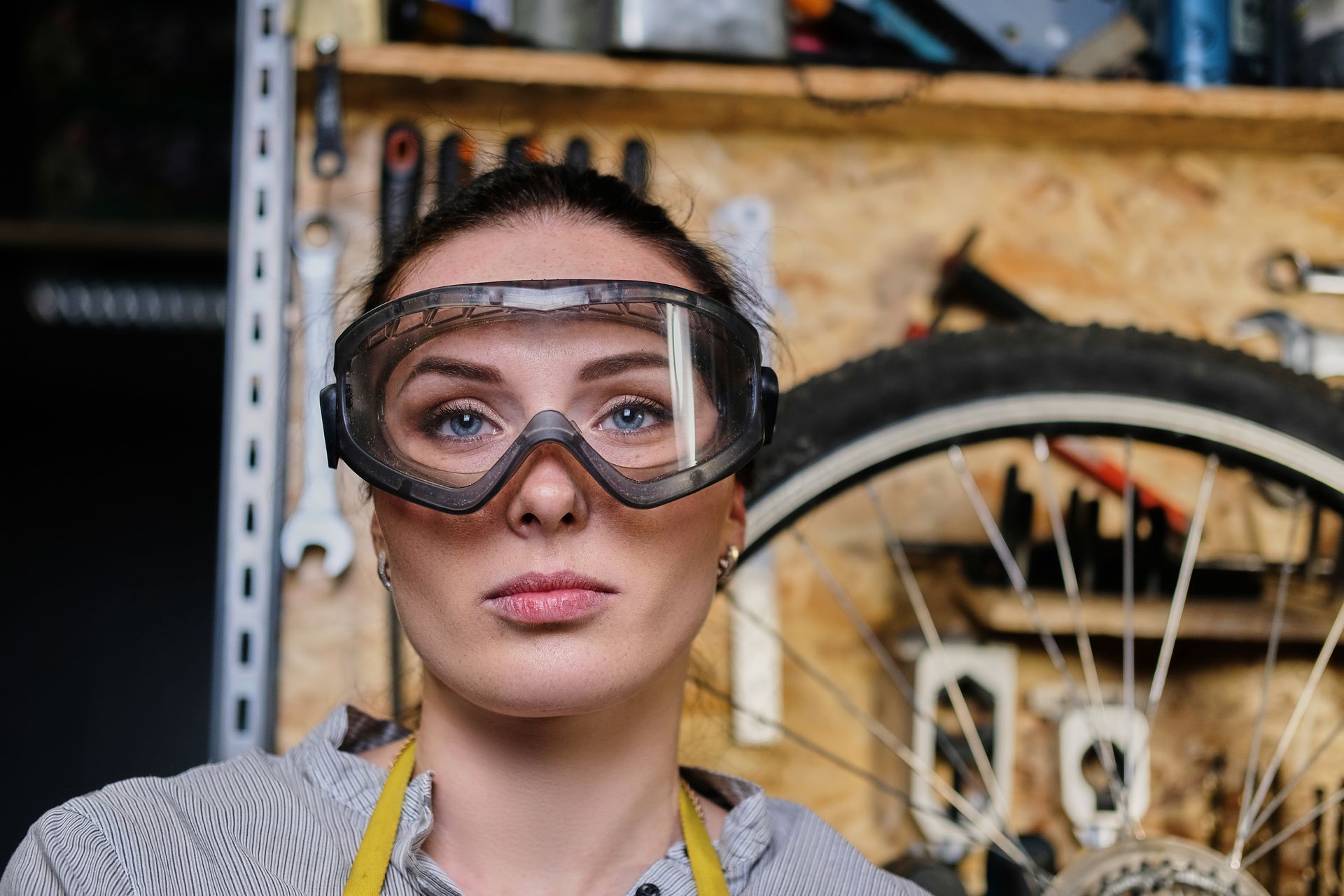 Person wearing safety goggles in a workshop, with a bicycle wheel and tools in the background