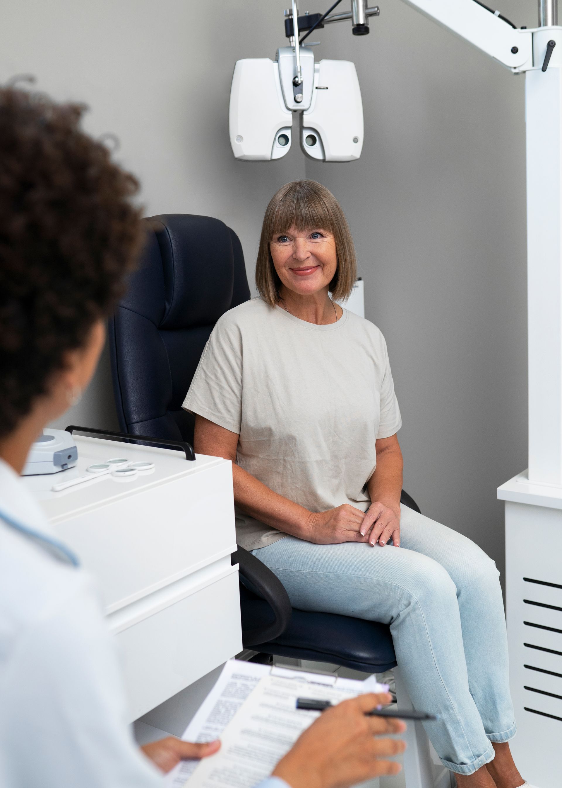 Patient seated in an eye exam chair while an optometrist reviews a chart
