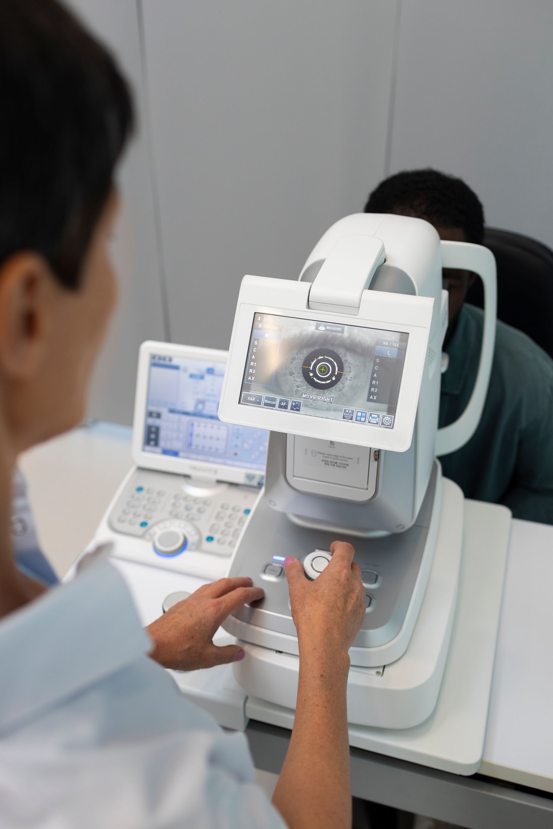 Technician examining a patient’s eye with a diagnostic imaging device in a clinic.