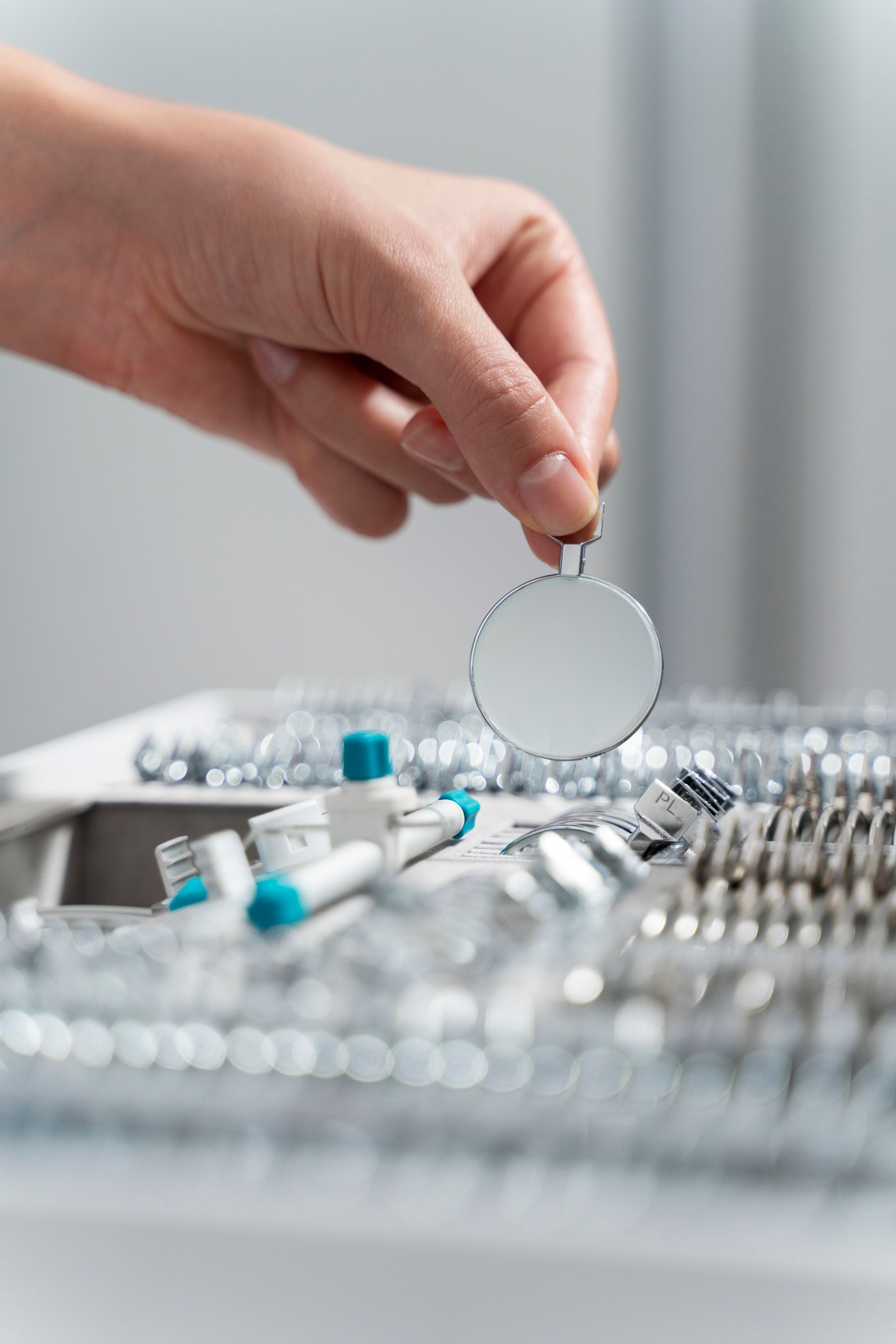 Hand placing a round dental mirror over assorted dental tools on a tray