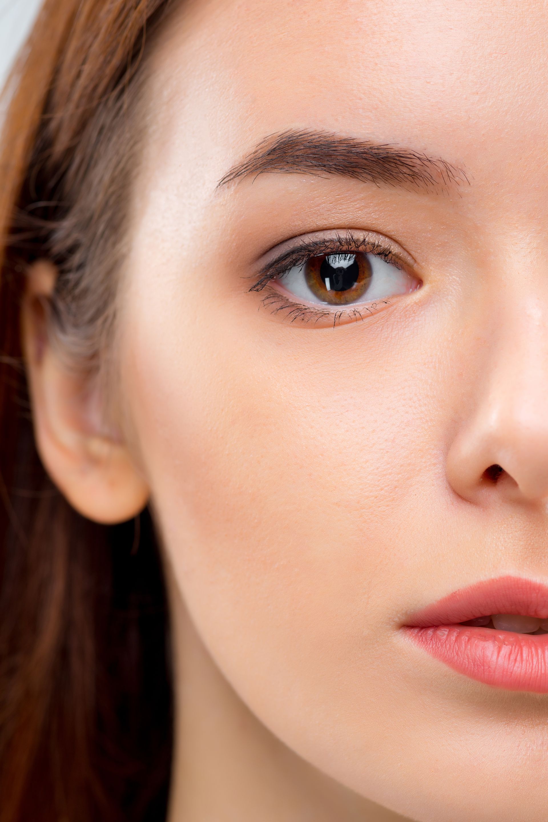 Close-up of a woman’s face with natural makeup and a neutral expression against a plain background