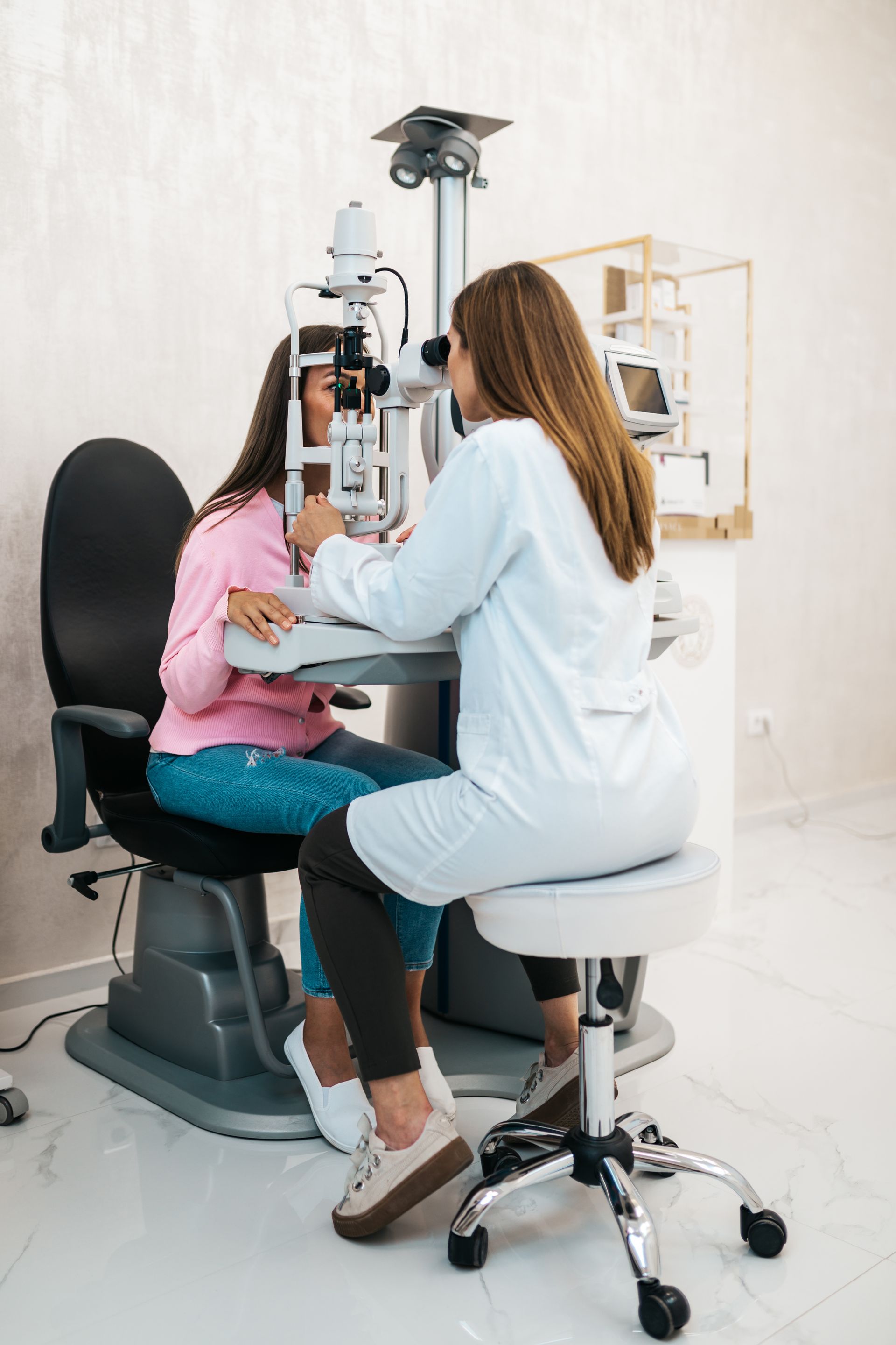 Eye exam in progress, with a patient seated at a vision testing machine and an optometrist examining her.