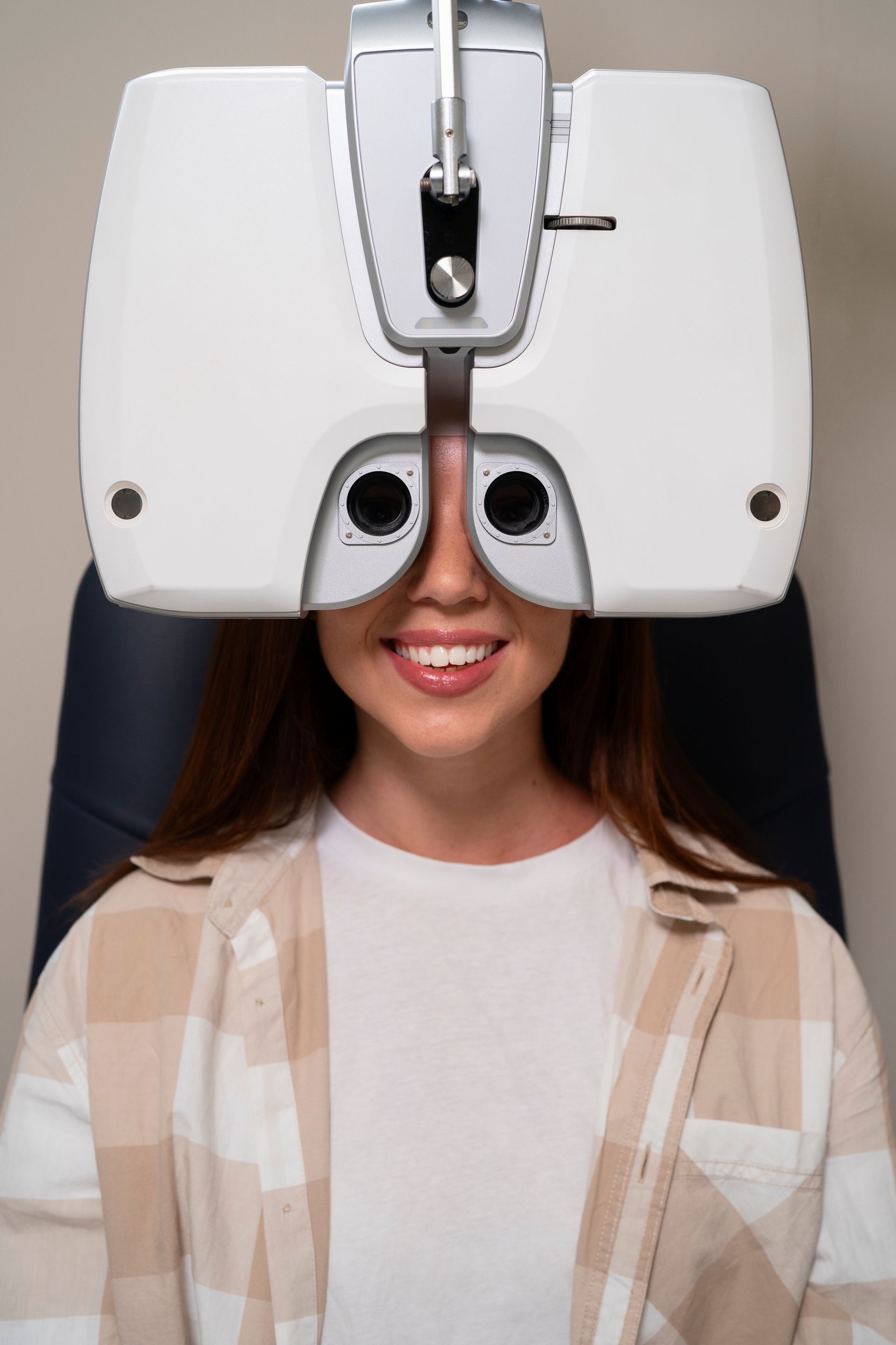 Woman using a white eye exam machine, smiling during an optometry test.