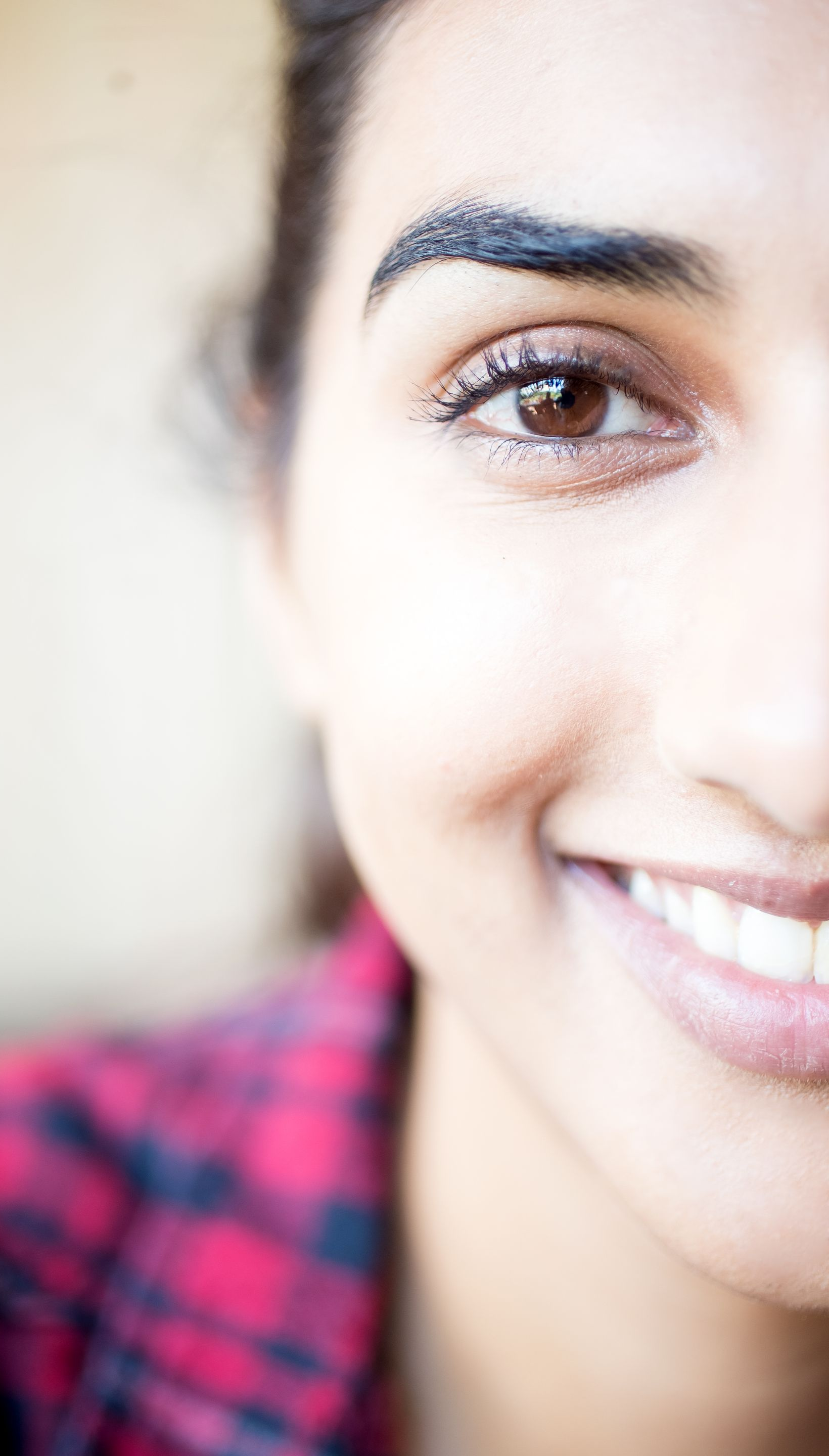 Close-up of a smiling person’s face, showing one eye and part of a red plaid shirt.