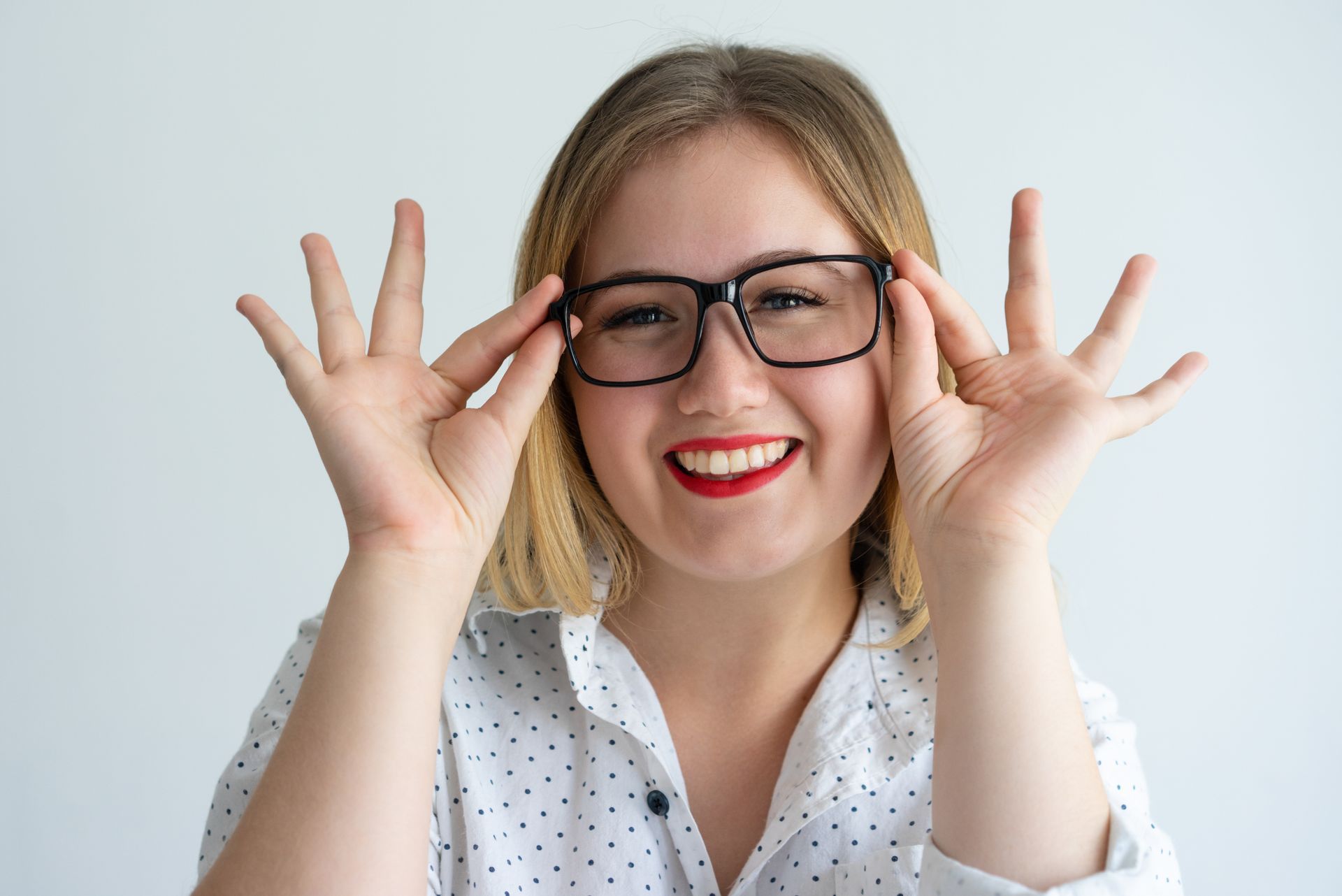 Smiling woman adjusting black glasses against a light gray background