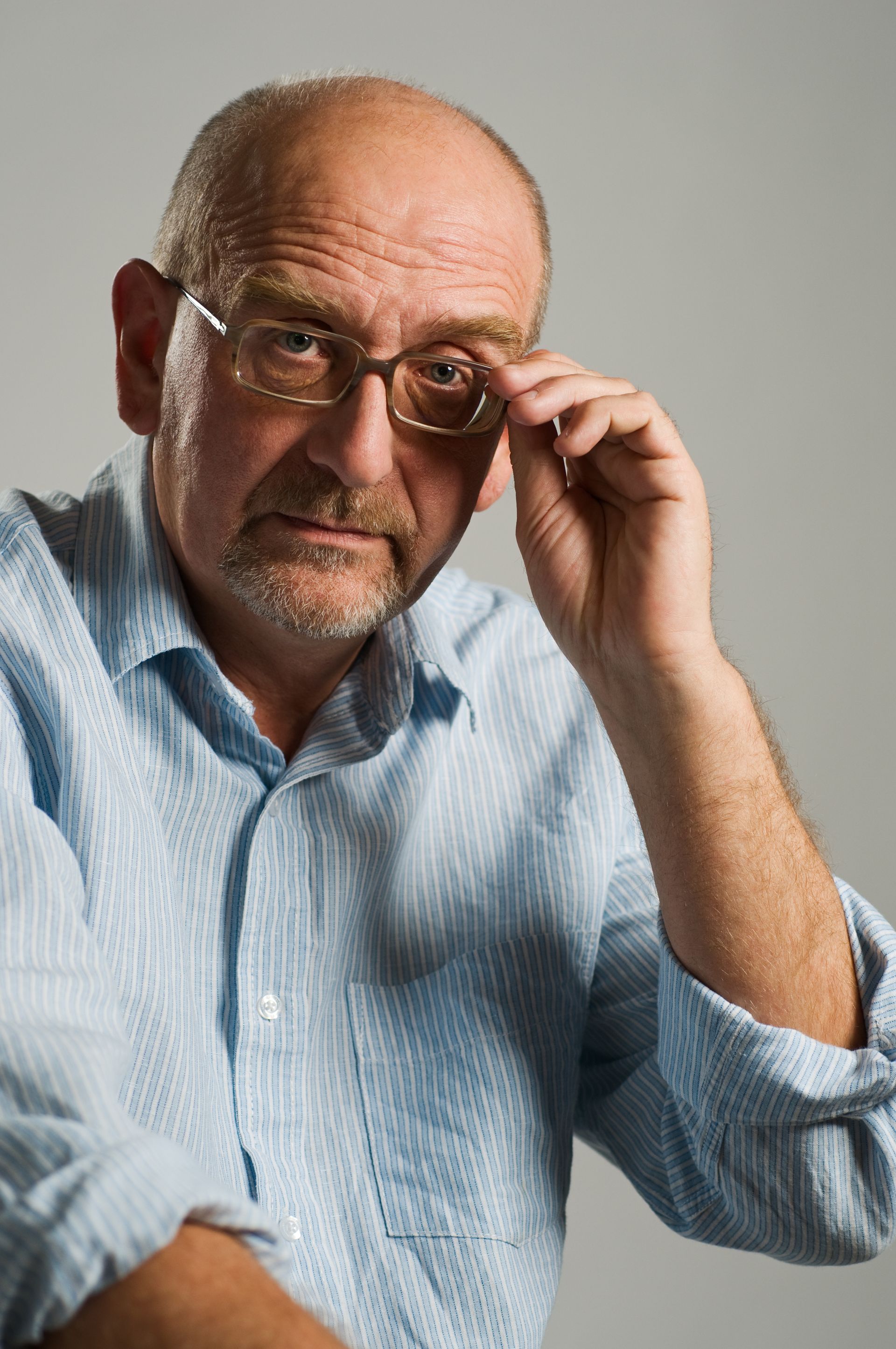 Man in a light blue shirt adjusting his glasses against a plain gray background