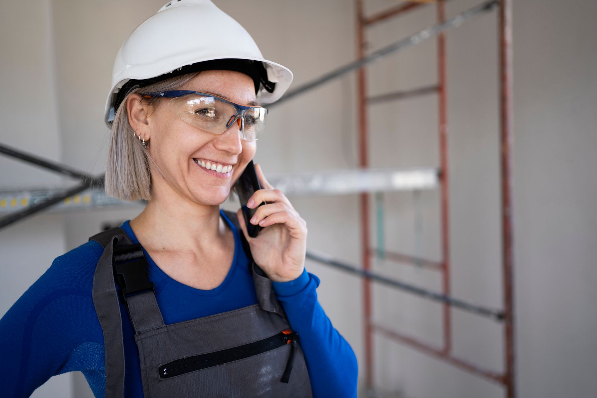 Construction worker in hard hat and safety glasses speaking on a phone at a building site