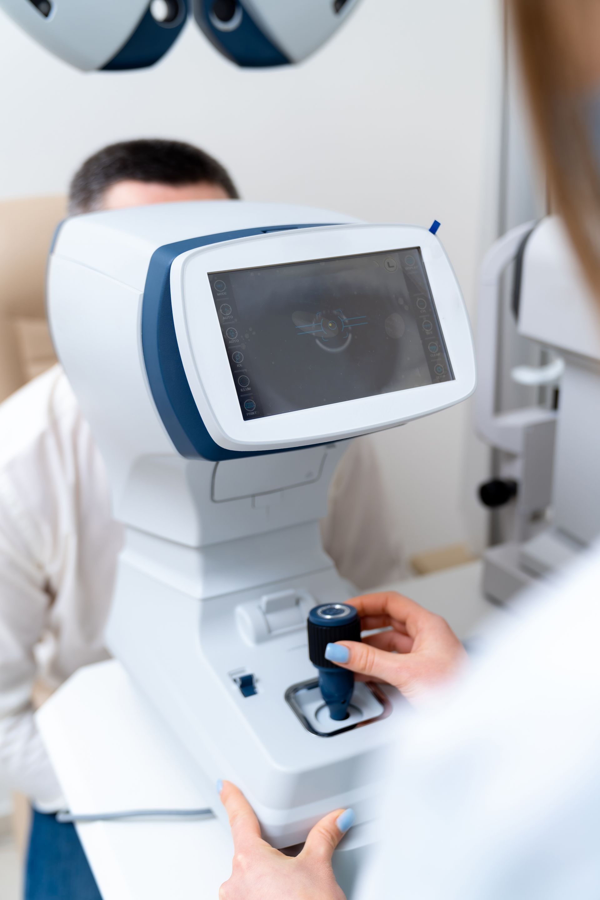 Person adjusting a blue-and-white eye exam device in a clinic